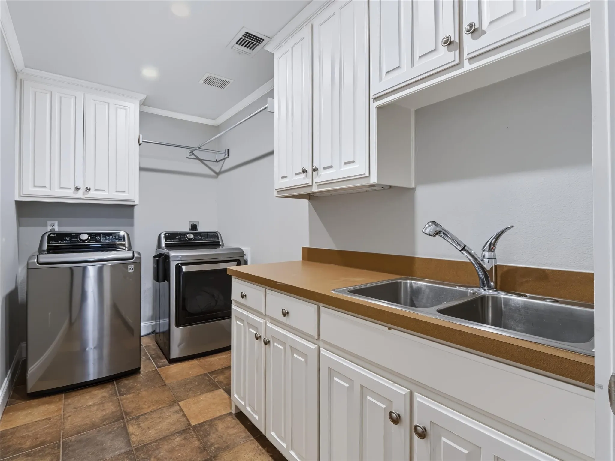 Laundry room featuring white cabinetry, a dual basin stainless steel sink, a pull-down faucet, and tile flooring