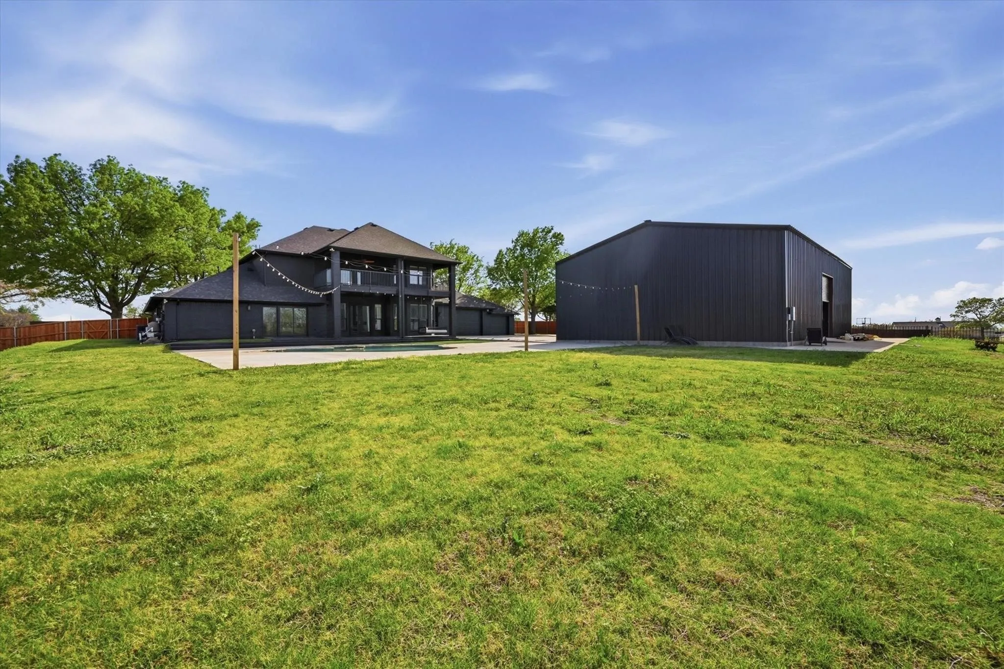 Spacious lawn with a multi-story residence featuring a covered balcony, large windows, and a separate structure with dark siding