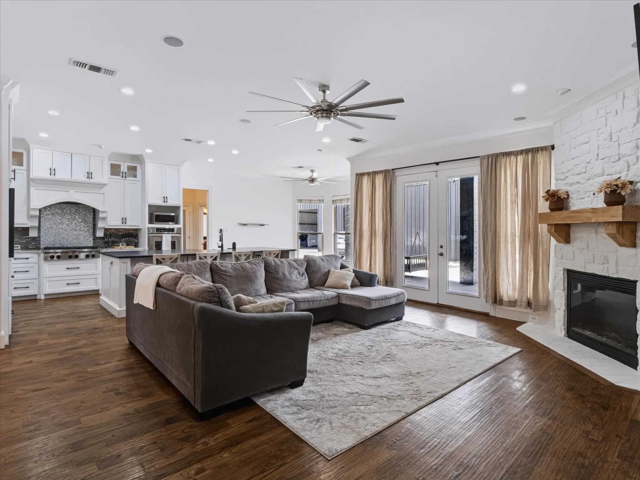 Gourmet kitchen with white cabinetry and dark countertops, wood-finish flooring, a white painted brick fireplace with a wood mantel, and double glass-paneled doors