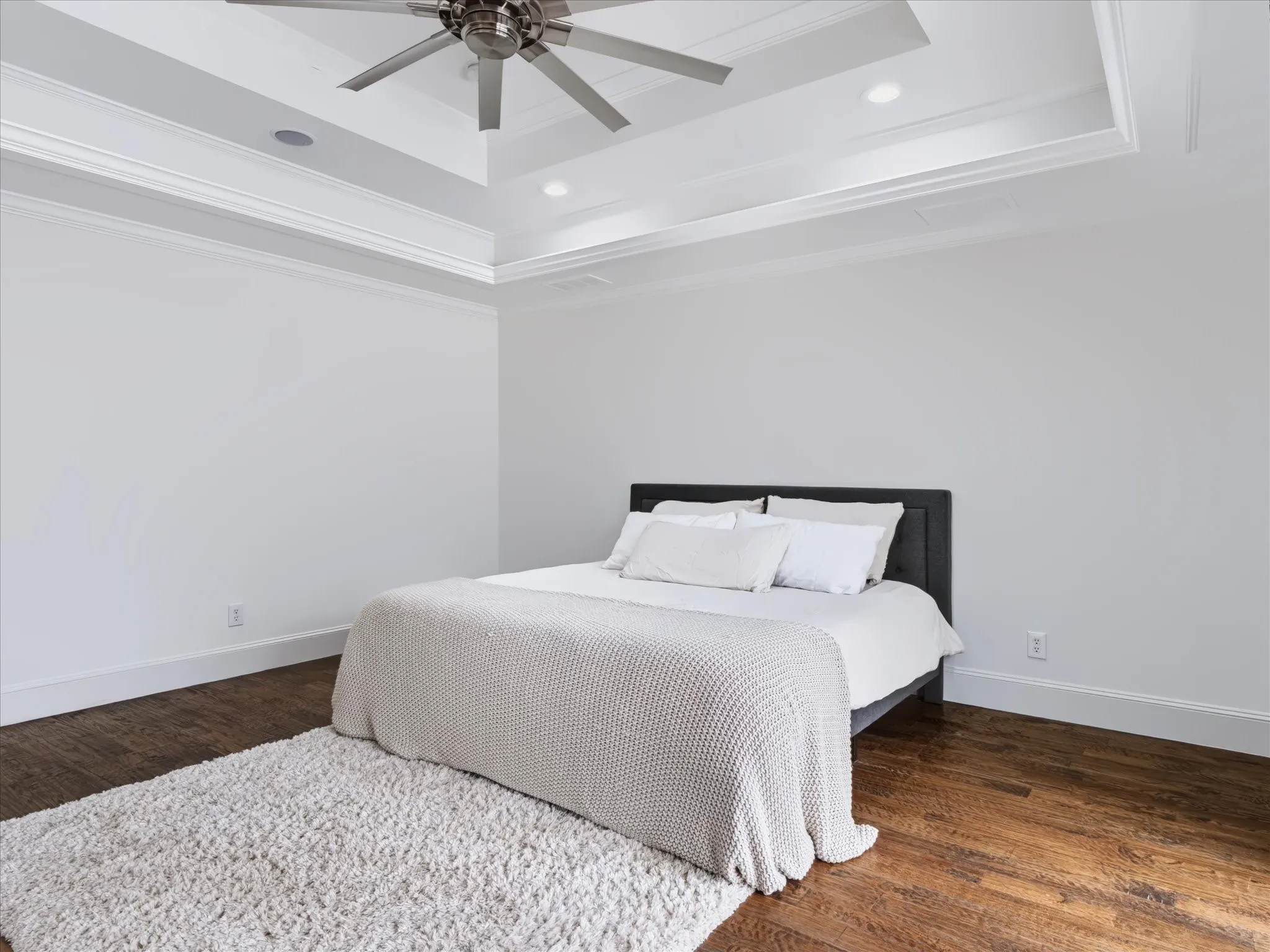 Tray ceiling with crown molding, recessed lighting, ceiling fan, and wood-finish flooring