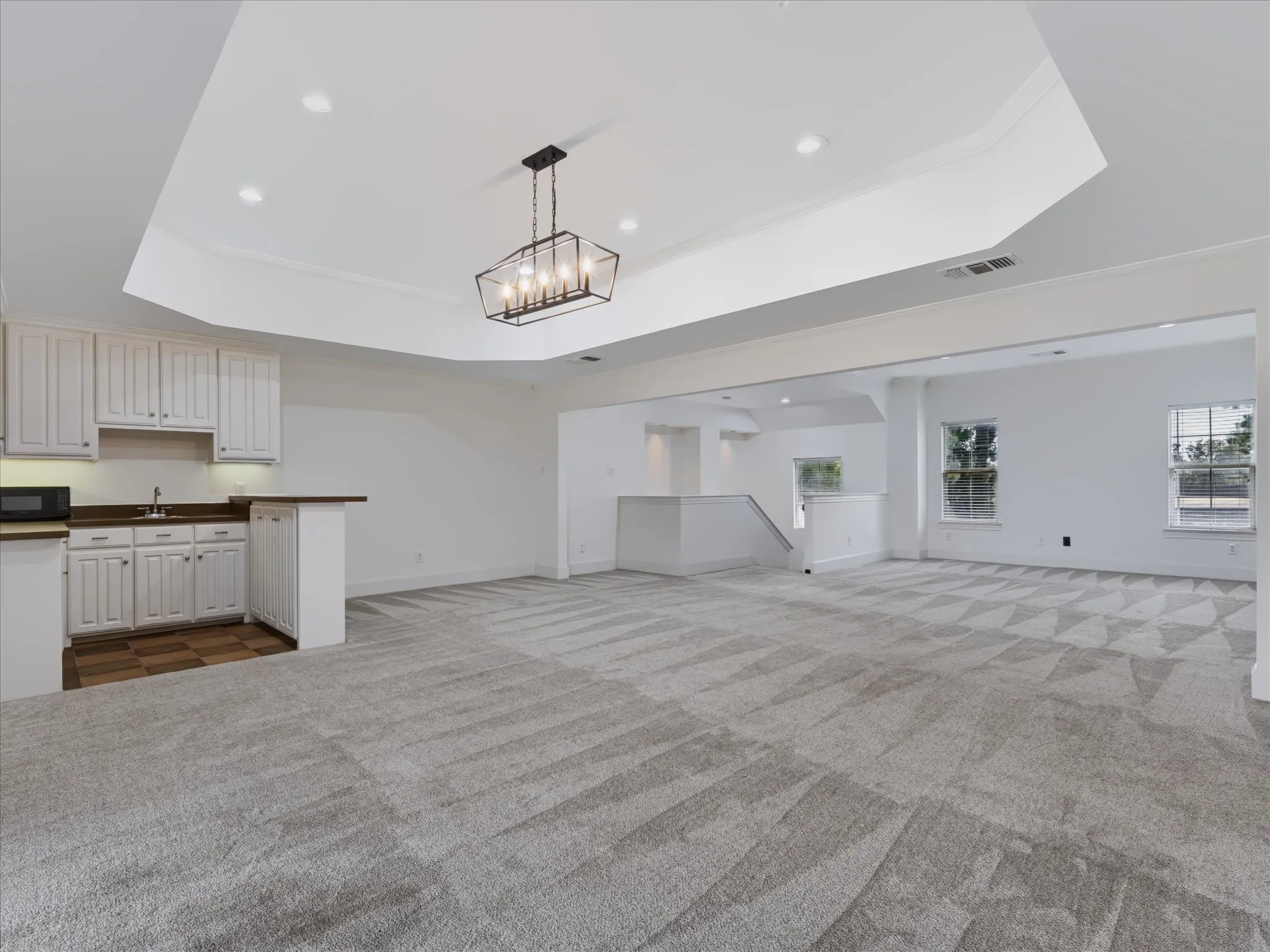 Expansive room featuring patterned carpet, a built-in wet bar with white cabinetry, a coffered ceiling with recessed lighting and a chandelier, and multiple windows