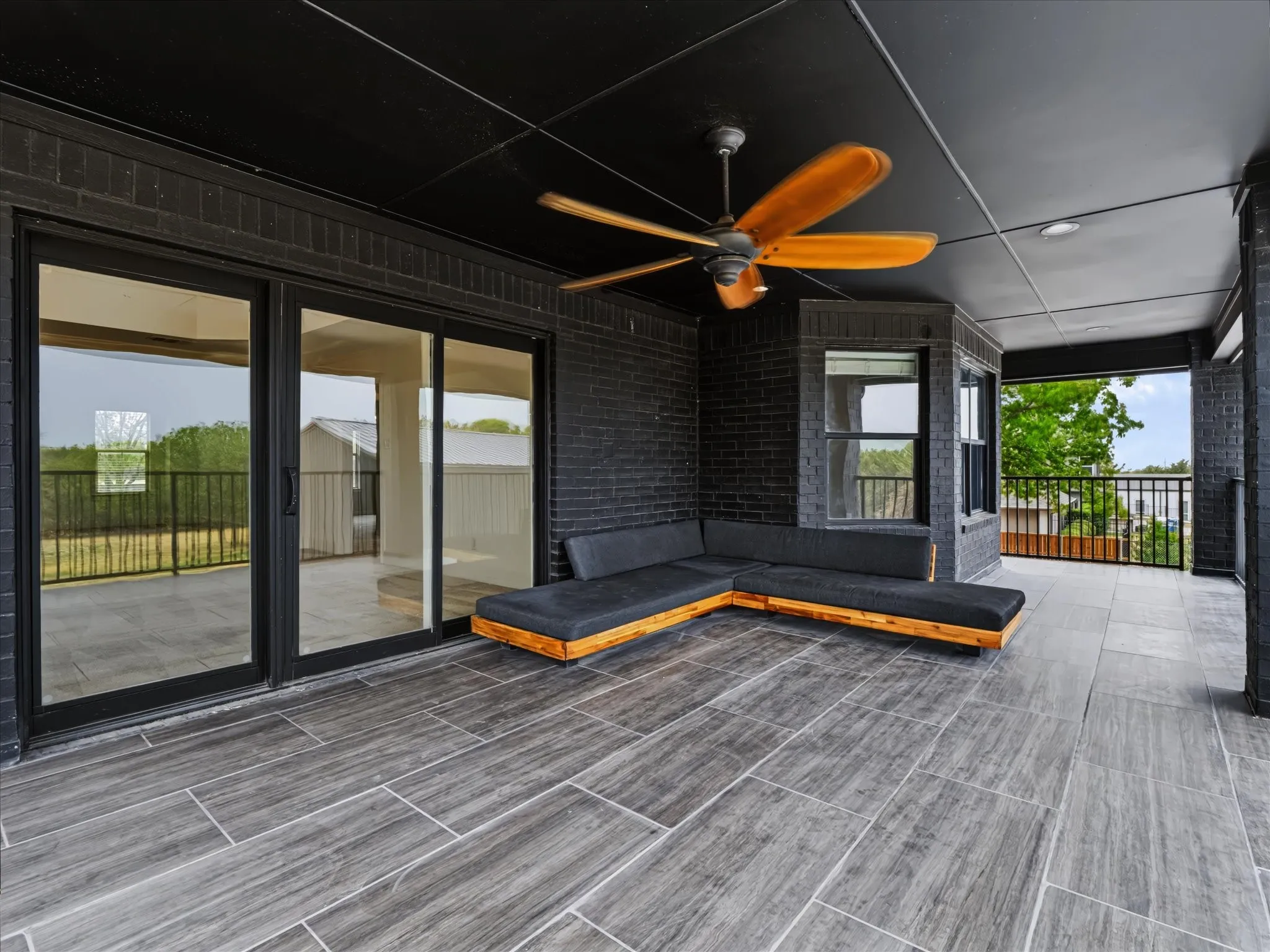 Covered outdoor living area featuring a large ceiling fan, dark brick wall accents, and wood-look tile flooring
