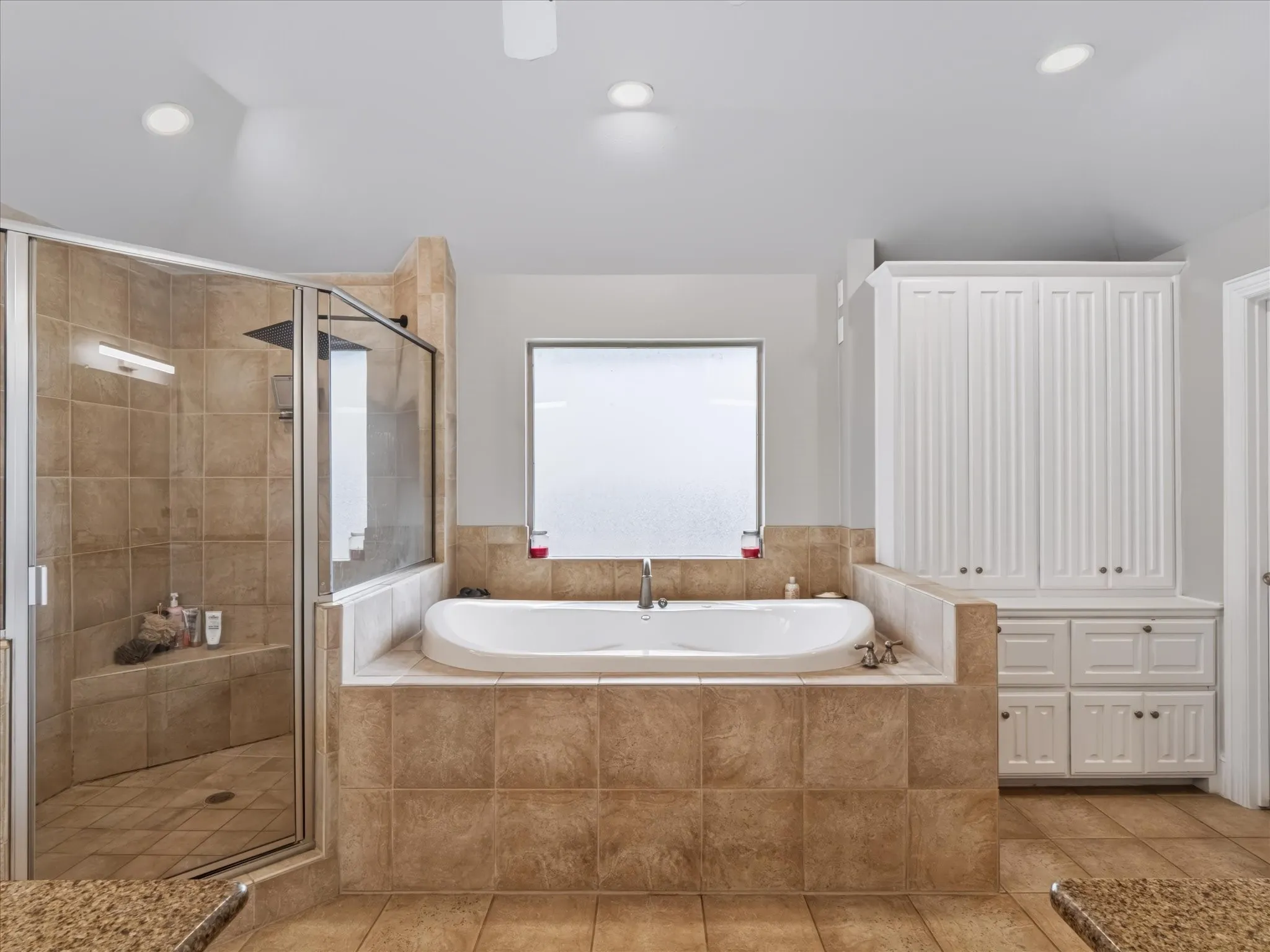 Spacious bathroom featuring a built-in soaking tub, a walk-in shower with a glass enclosure, an integrated shower bench, and extensive built-in white cabinetry with beadboard detailing