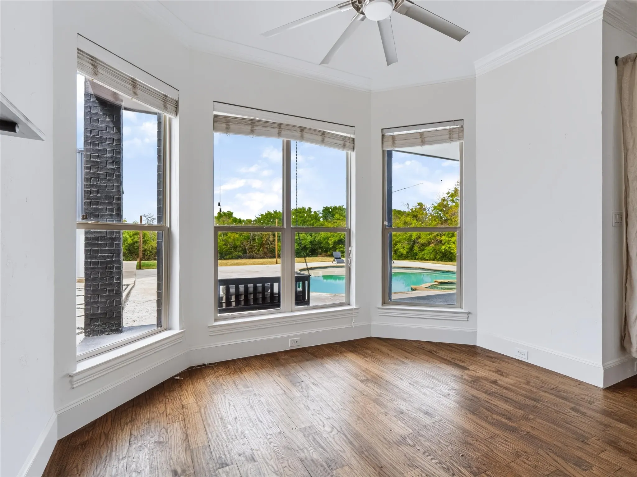 Bay window arrangement with wood-finish flooring, ceiling fan, and crown molding