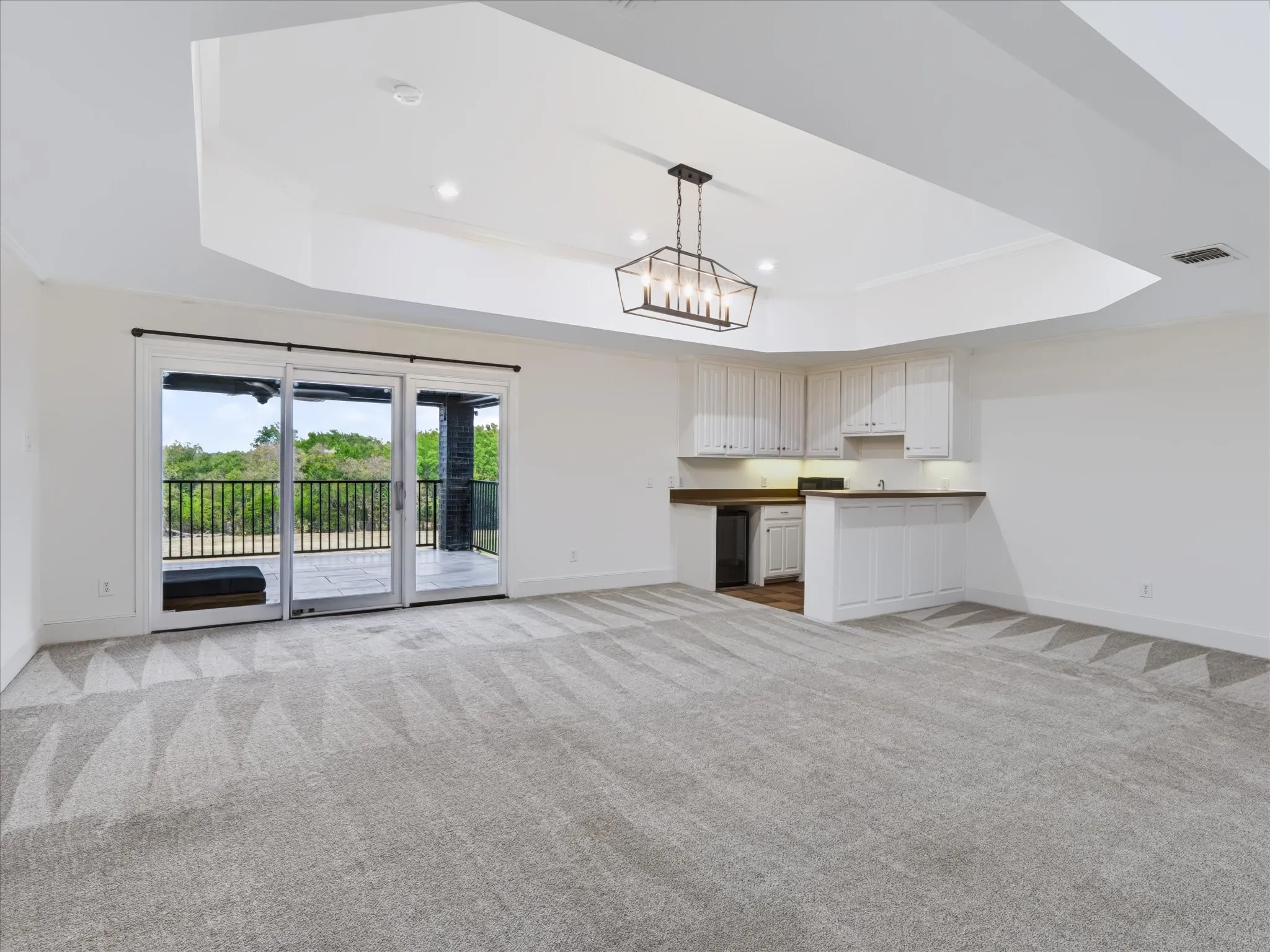 Spacious room featuring carpeting, a built-in wet bar with white cabinetry and dark countertops, and sliding glass doors with direct outdoor access