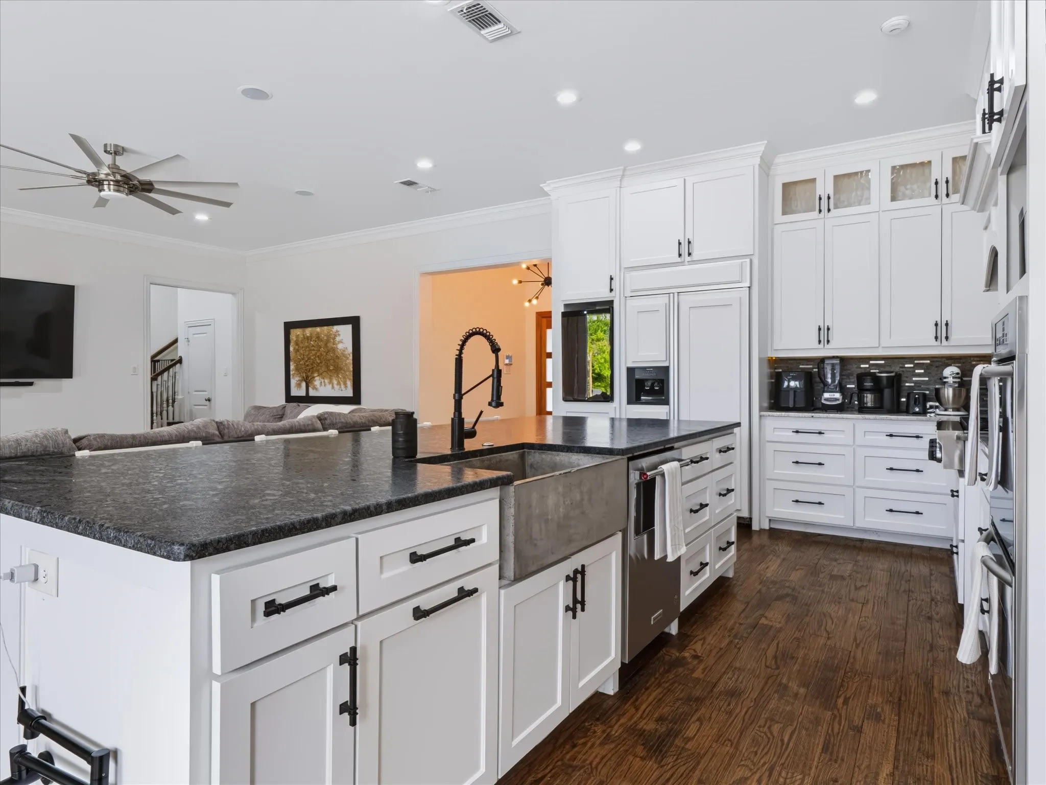 White shaker cabinetry with black hardware, dark wood-finish flooring, recessed lighting, concrete apron-front sink, and integrated appliances