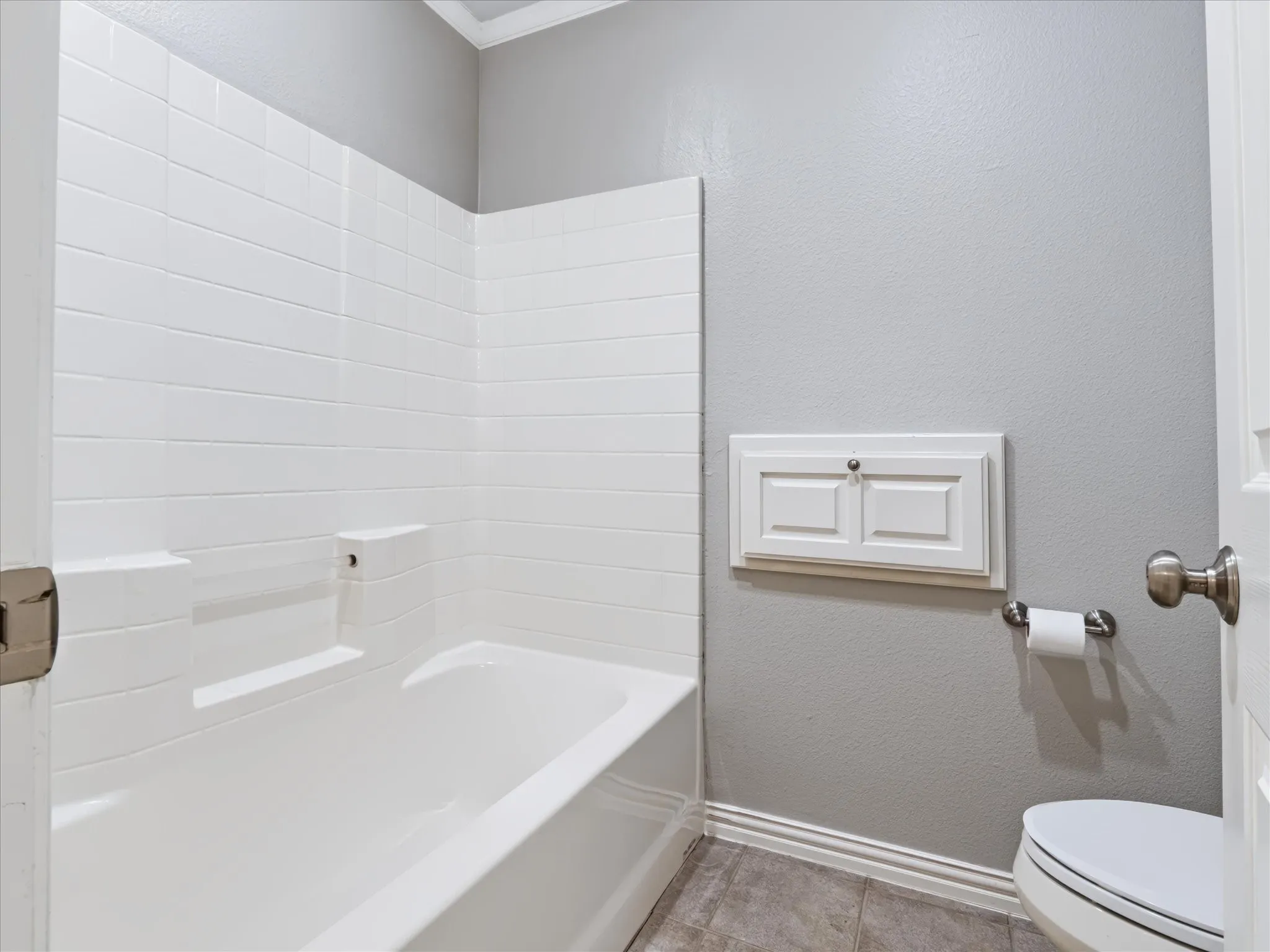 White subway tile shower surround, built-in tub, built-in storage cabinet, and tile flooring