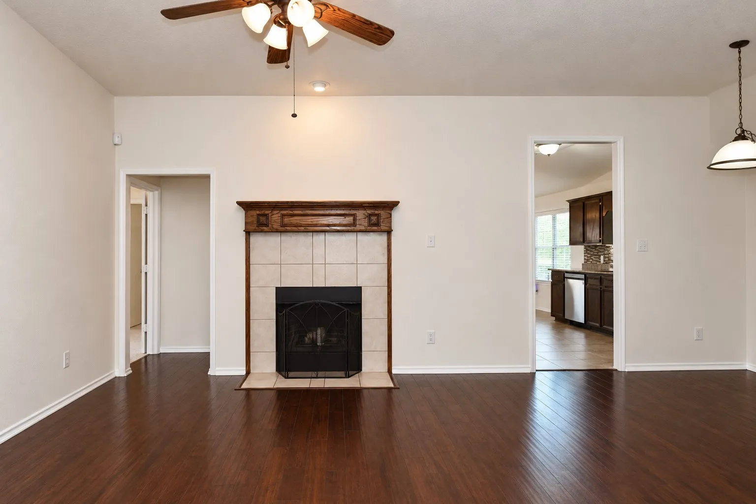 Wood-finish flooring, tiled fireplace with carved wood mantel, recessed lighting, ceiling fan light fixture, and pendant light fixture