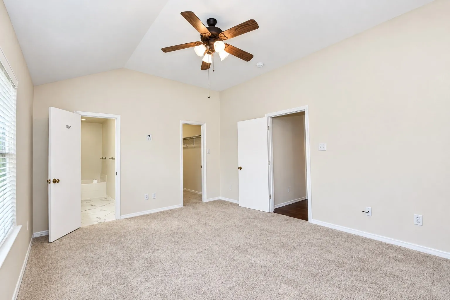 Vaulted ceiling with a ceiling fan, plush carpet, window with blinds, and white doors leading to additional spaces