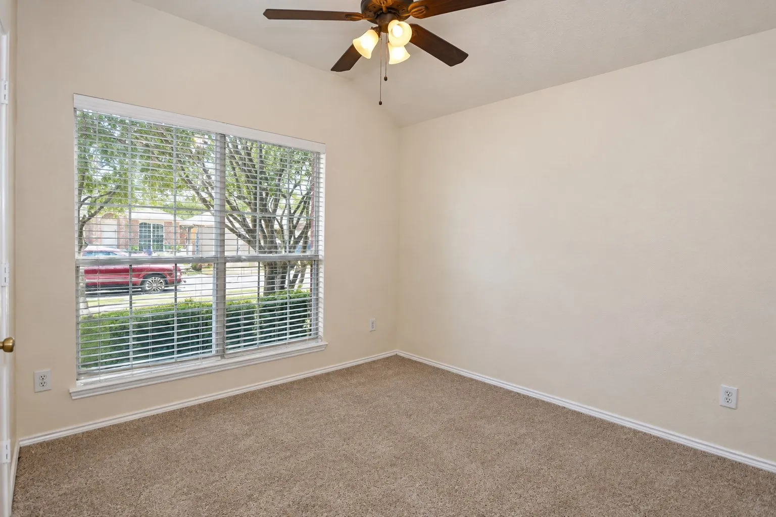 Carpeted flooring, vaulted ceiling, ceiling fan with integrated lighting, large window with blinds, and light-toned wall finishes