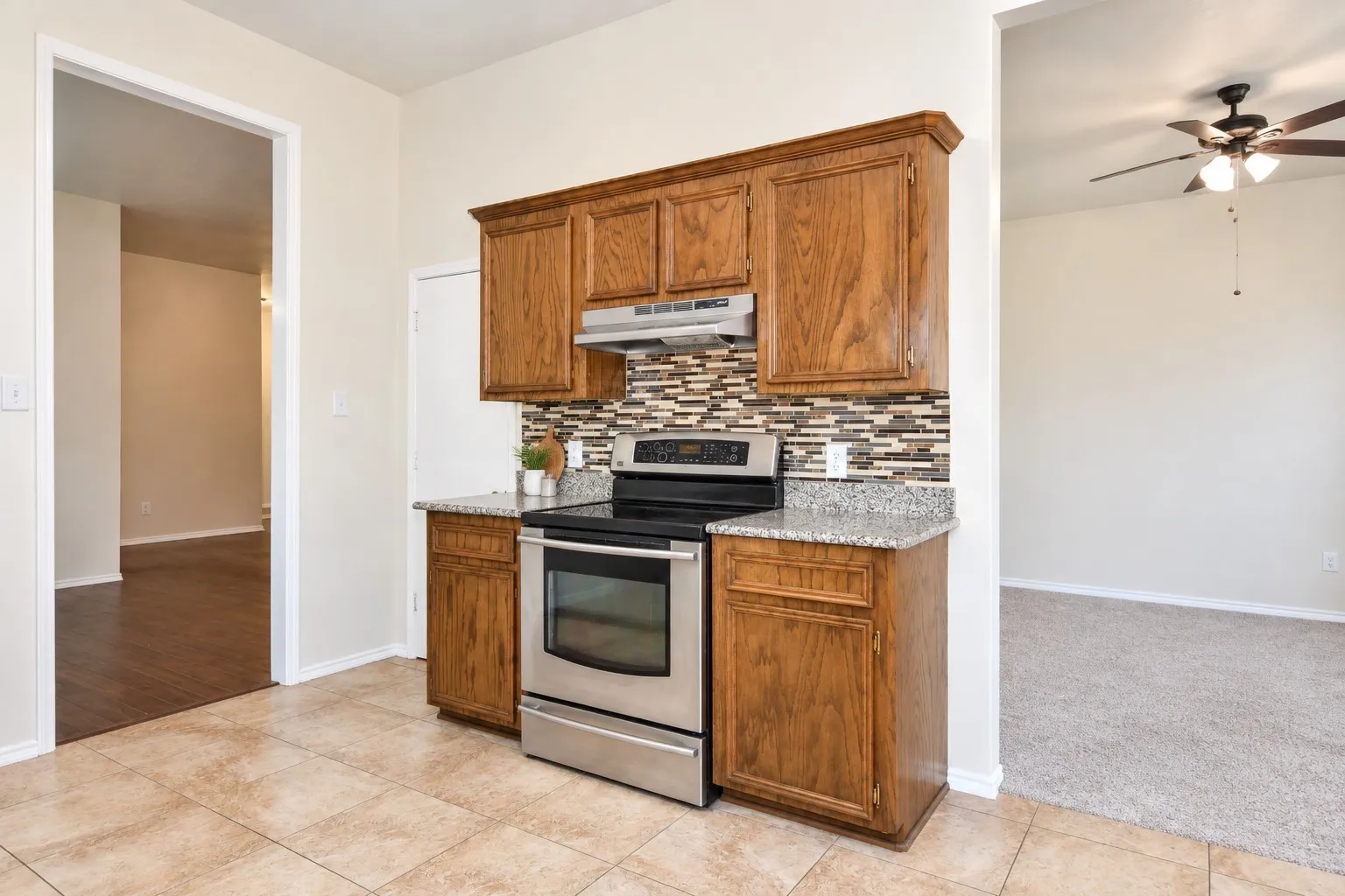 Stainless steel oven and range with overhead microwave, natural wood-finish cabinetry, mosaic tile backsplash, and stone-finish countertops