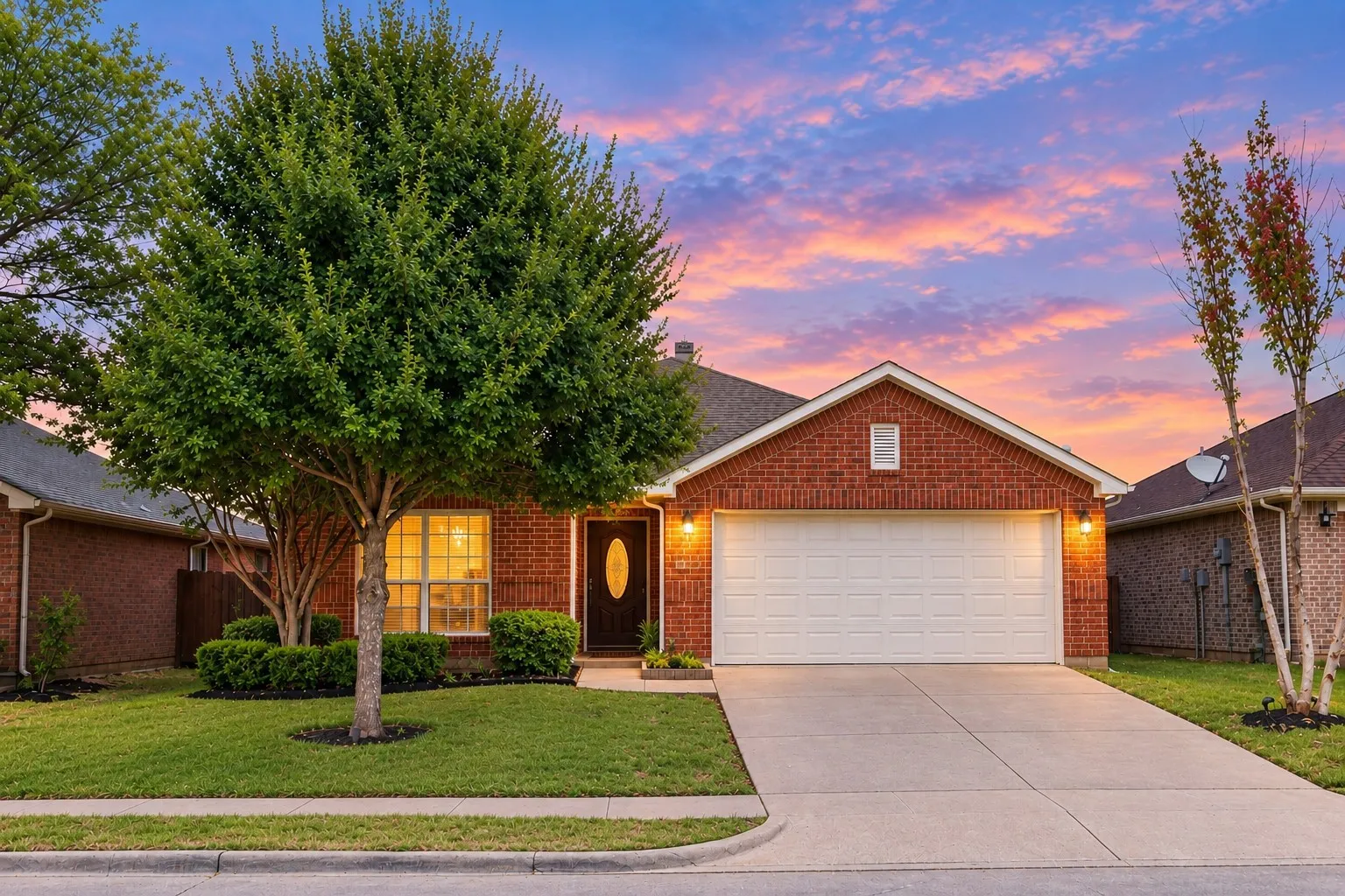 Brick exterior with a gabled roofline, concrete driveway, attached garage, and mature landscaping