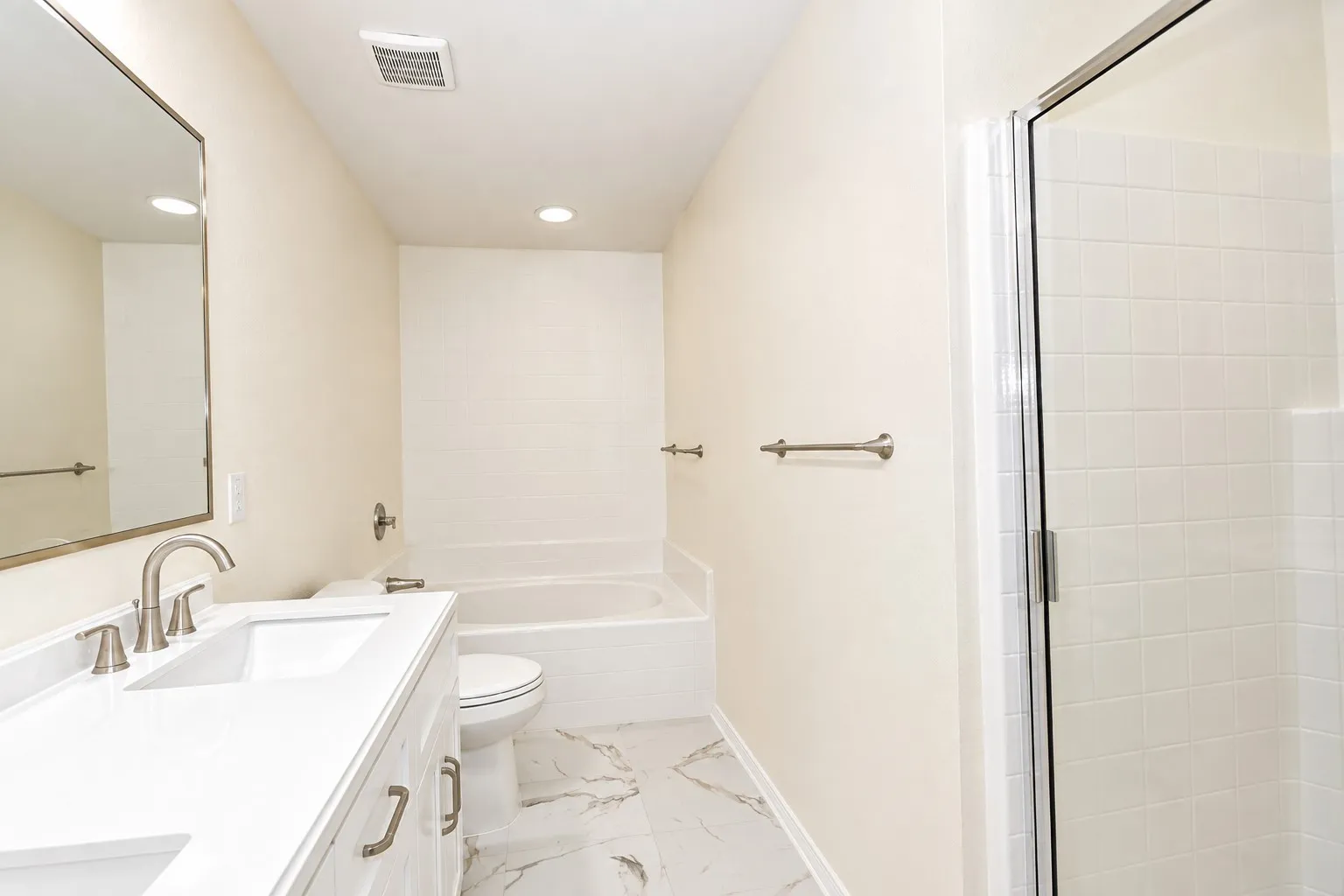 White vanity with integrated sink, brushed nickel fixtures, and a glass-enclosed shower