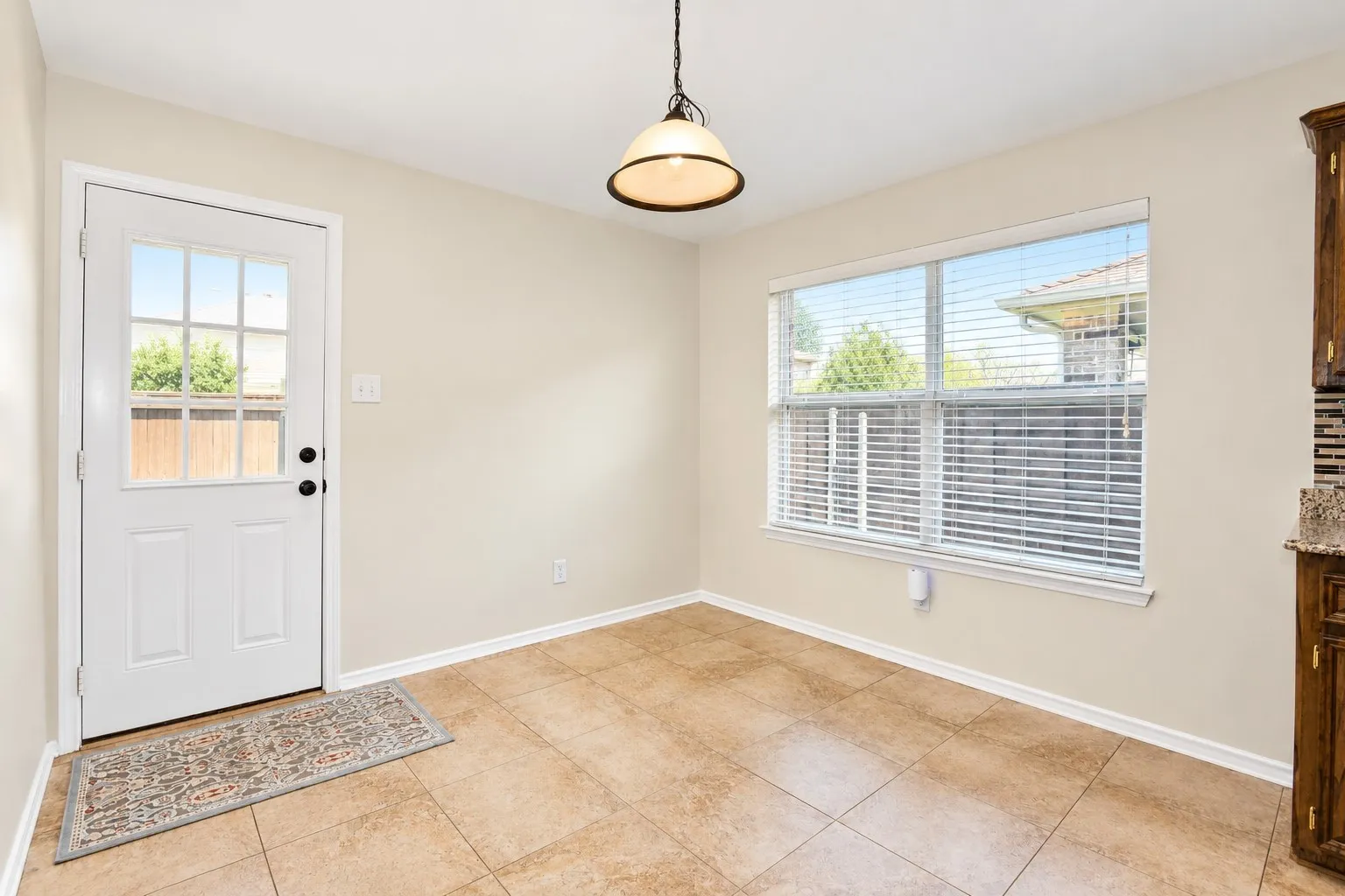 Tile flooring, white paneled door with glass inserts, single-hung window with blinds, overhead pendant light fixture, and built-in cabinetry with granite countertop and tile backsplash