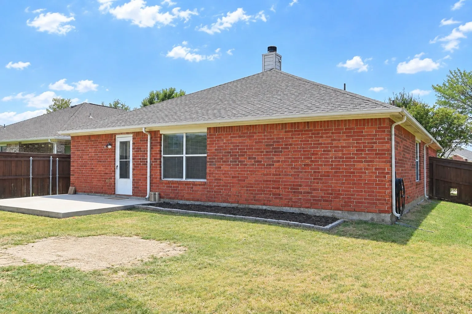 Brick exterior with a concrete patio, a chimney, and a privacy fence