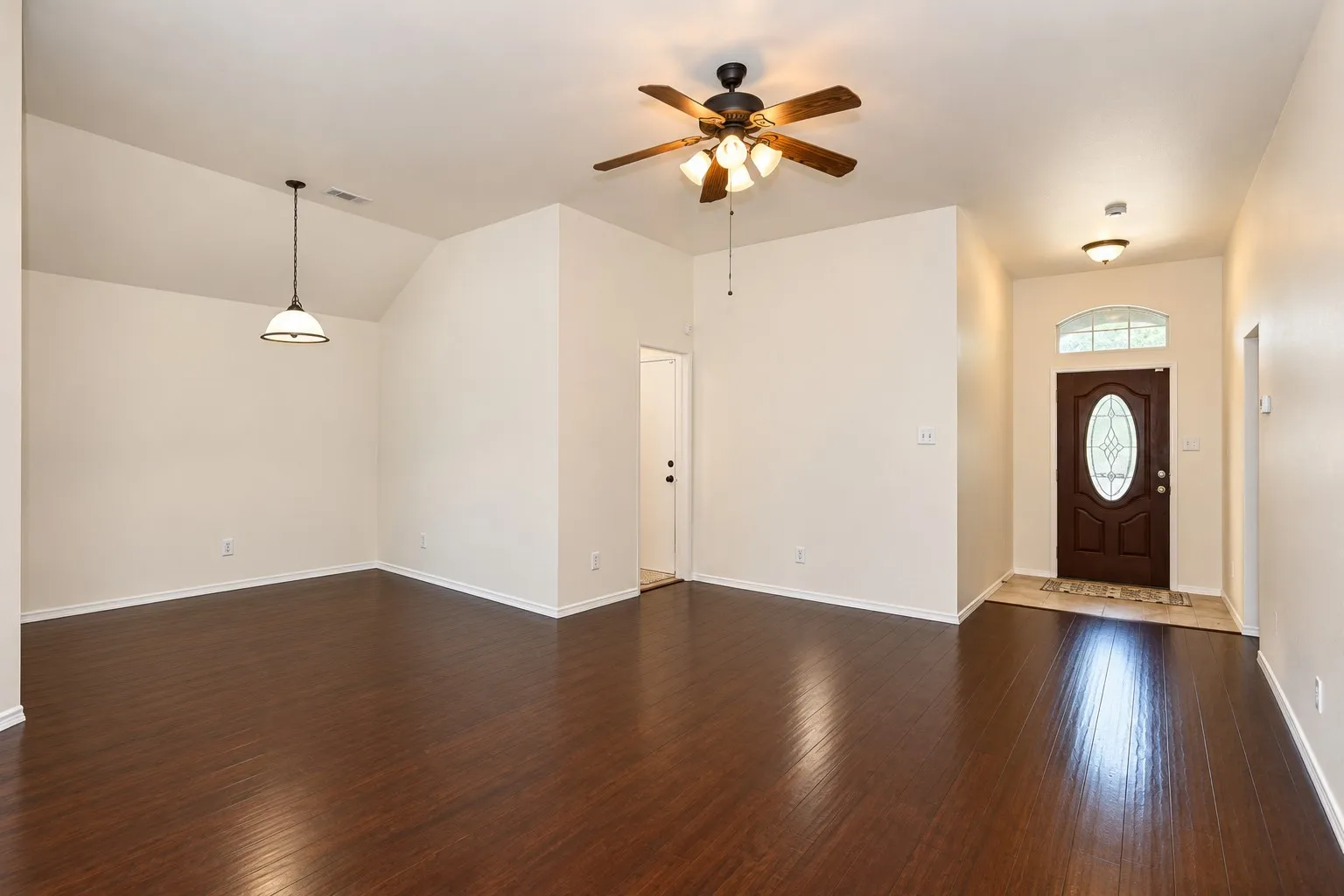 Wood-finish flooring, vaulted ceiling, ceiling fan, decorative front door with arched transom, and pendant lighting