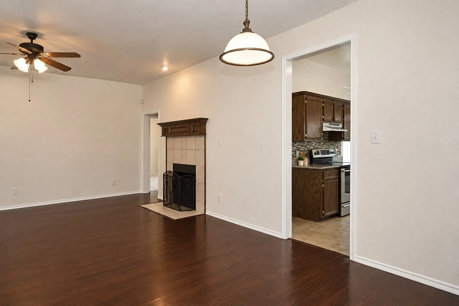 Wood-finish flooring, ceiling fan, fireplace with tile surround, built-in recessed lighting, and a transitional pendant light fixture