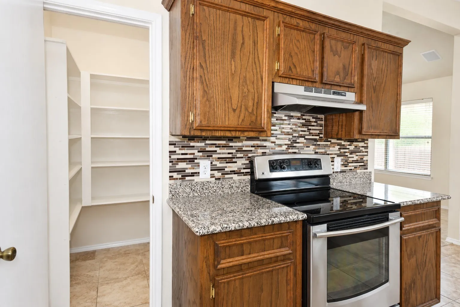 Wood-finish cabinetry paired with granite-style countertops, stainless steel range and range hood, and a mosaic tile backsplash