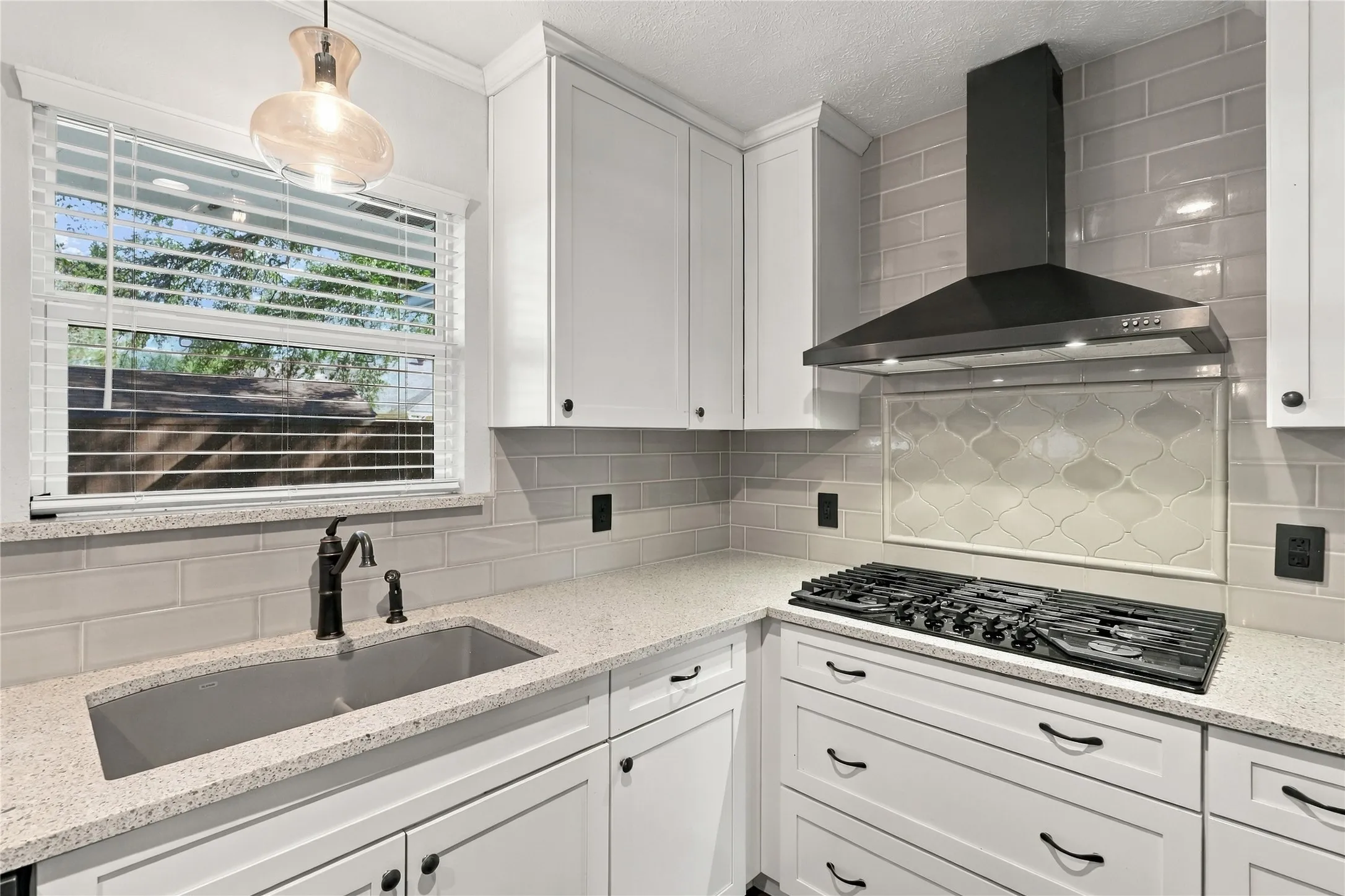 White shaker cabinetry, light-toned countertops, gas cooktop, black range hood, and subway tile backsplash