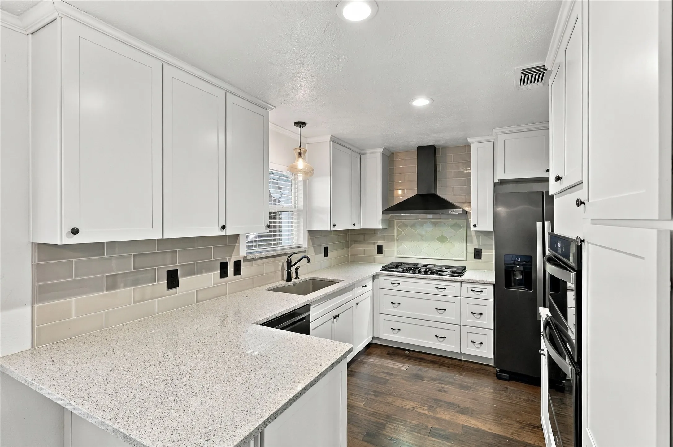 White shaker cabinetry, light-toned countertops, subway tile backsplash, dark wood-finish flooring, and stainless steel appliances