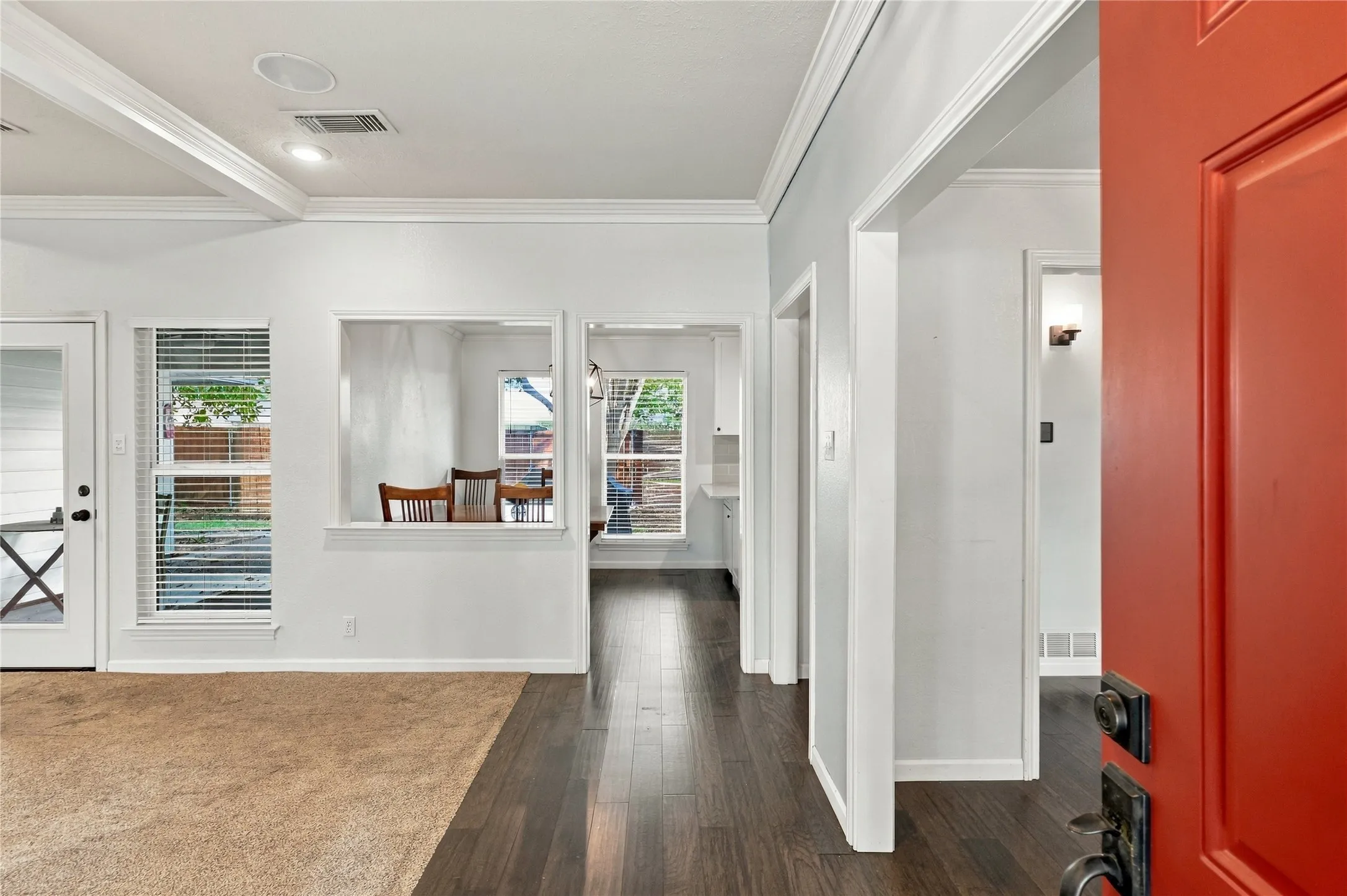 Red entry door opening to an interior featuring recessed lighting, crown molding, and a combination of carpet and wood-finish flooring
