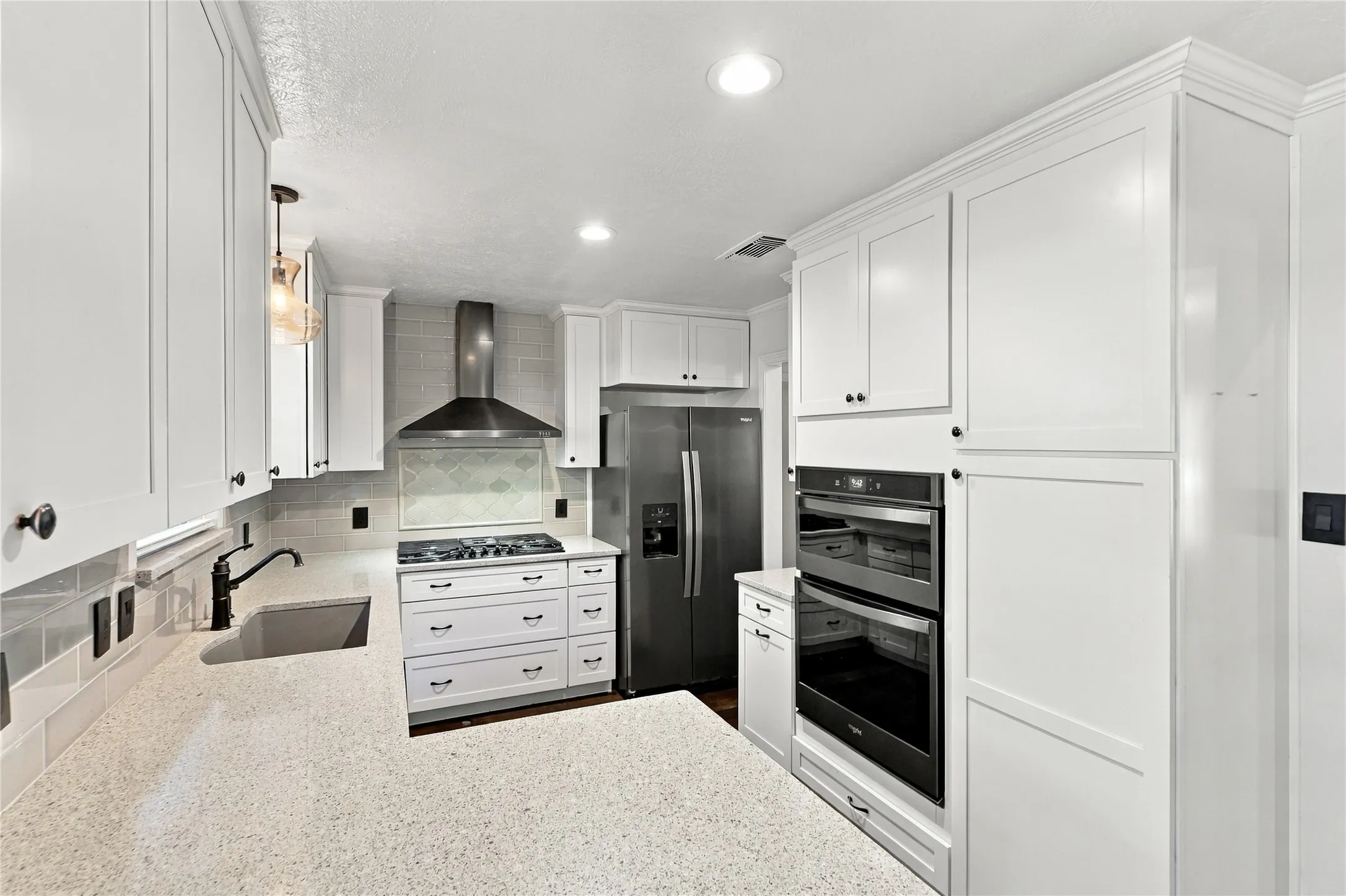 White shaker-style cabinetry, stainless steel appliances, quartz countertops, tile backsplash, and recessed lighting