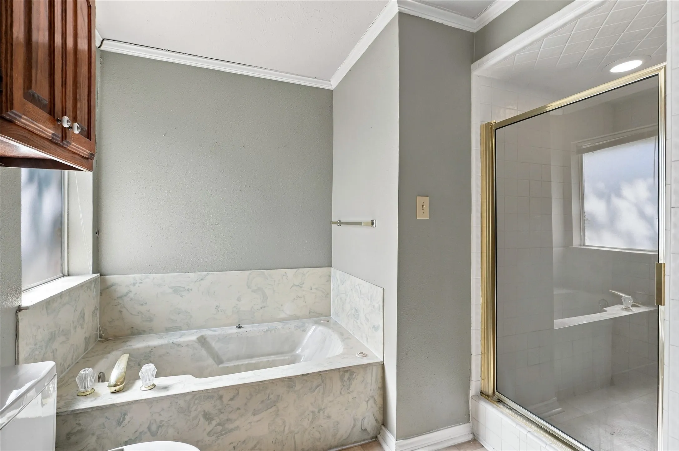 Built-in soaking tub with a stone-finish surround, glass-enclosed shower, wall-mounted towel bar, and wood-finish cabinetry