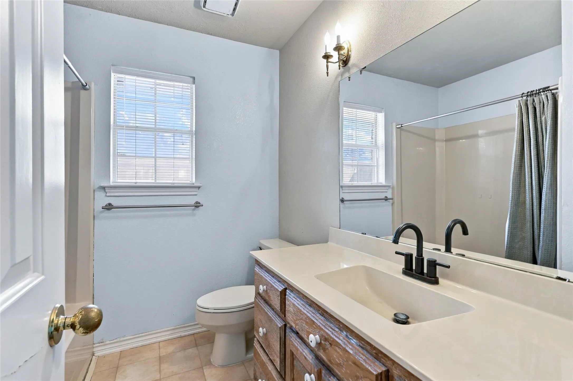 Light-toned wall paint with a window, vanity with a light-colored countertop, built-in sink, and a black-finish faucet
