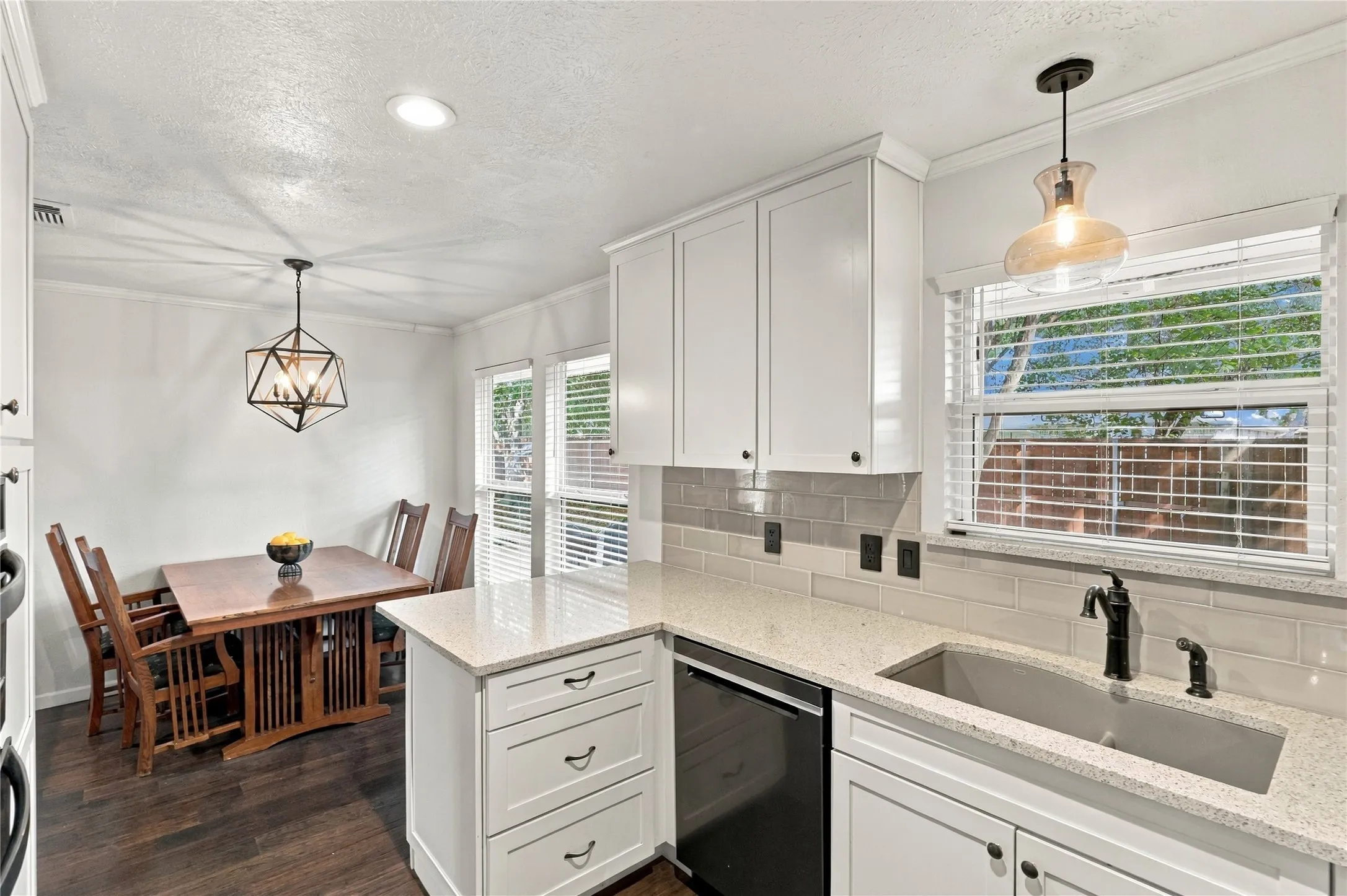 White cabinetry with dark hardware, stone countertops, subway tile backsplash, stainless steel sink with a dark faucet, and wood-finish​​‌​​​​‌​​‌‌​‌‌​​​‌‌​‌​‌​‌​​​‌​​ flooring