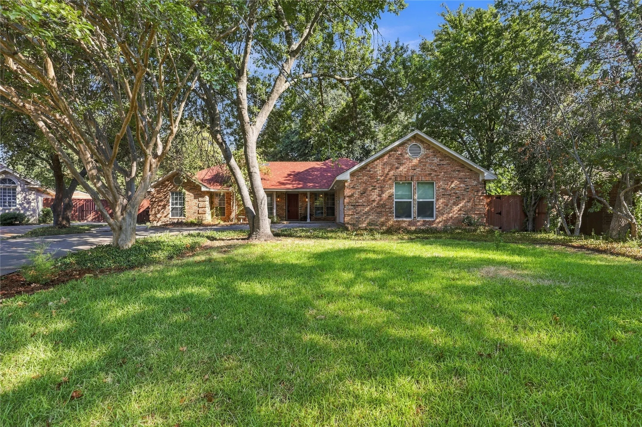 Brick exterior with a red roof, front yard, and mature trees