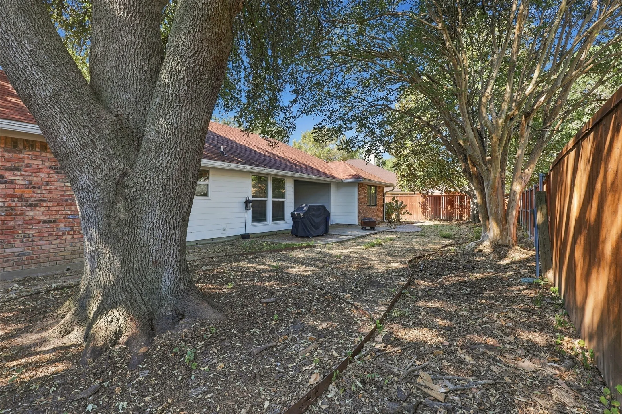 Spacious backyard featuring mature trees, a red brick exterior, white siding, and a wood privacy fence