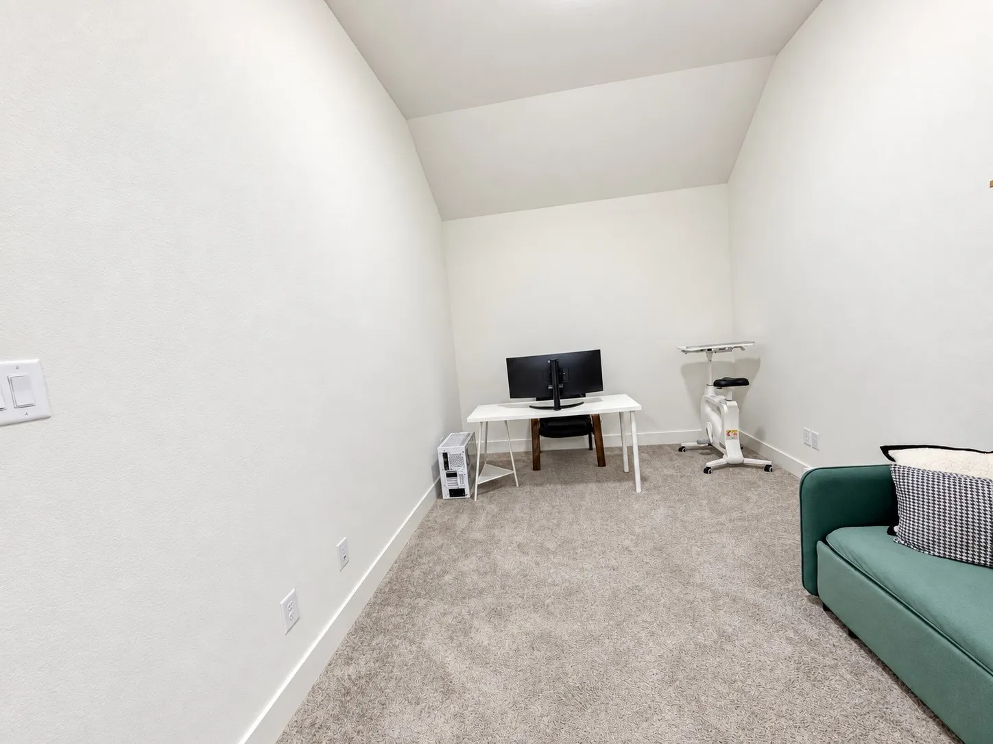Neutral-toned carpet flooring, white painted walls, and an angled ceiling
