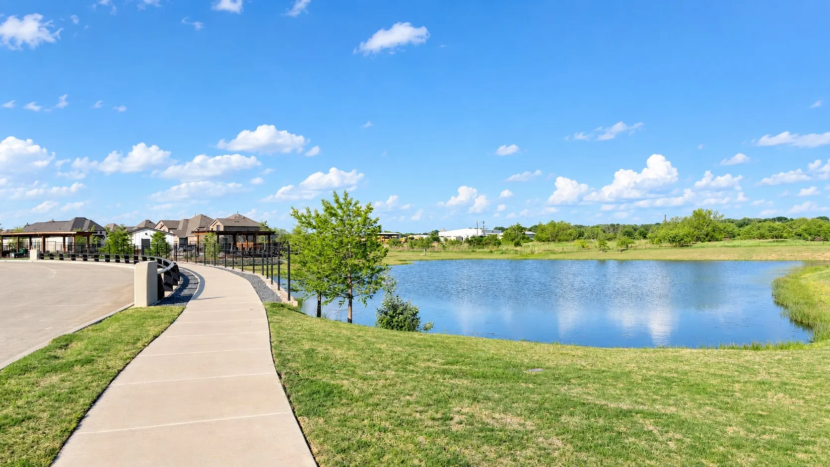 Waterfront setting featuring a paved pathway, manicured lawn, and lush landscaping