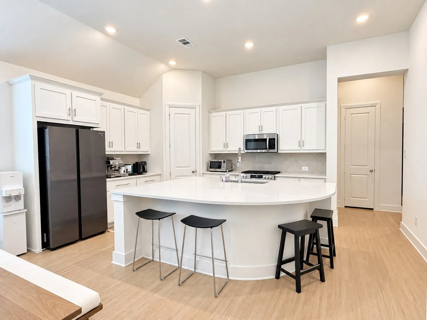 White shaker cabinetry with brushed nickel hardware, stainless steel appliances, solid surface countertops, and light wood-finish flooring