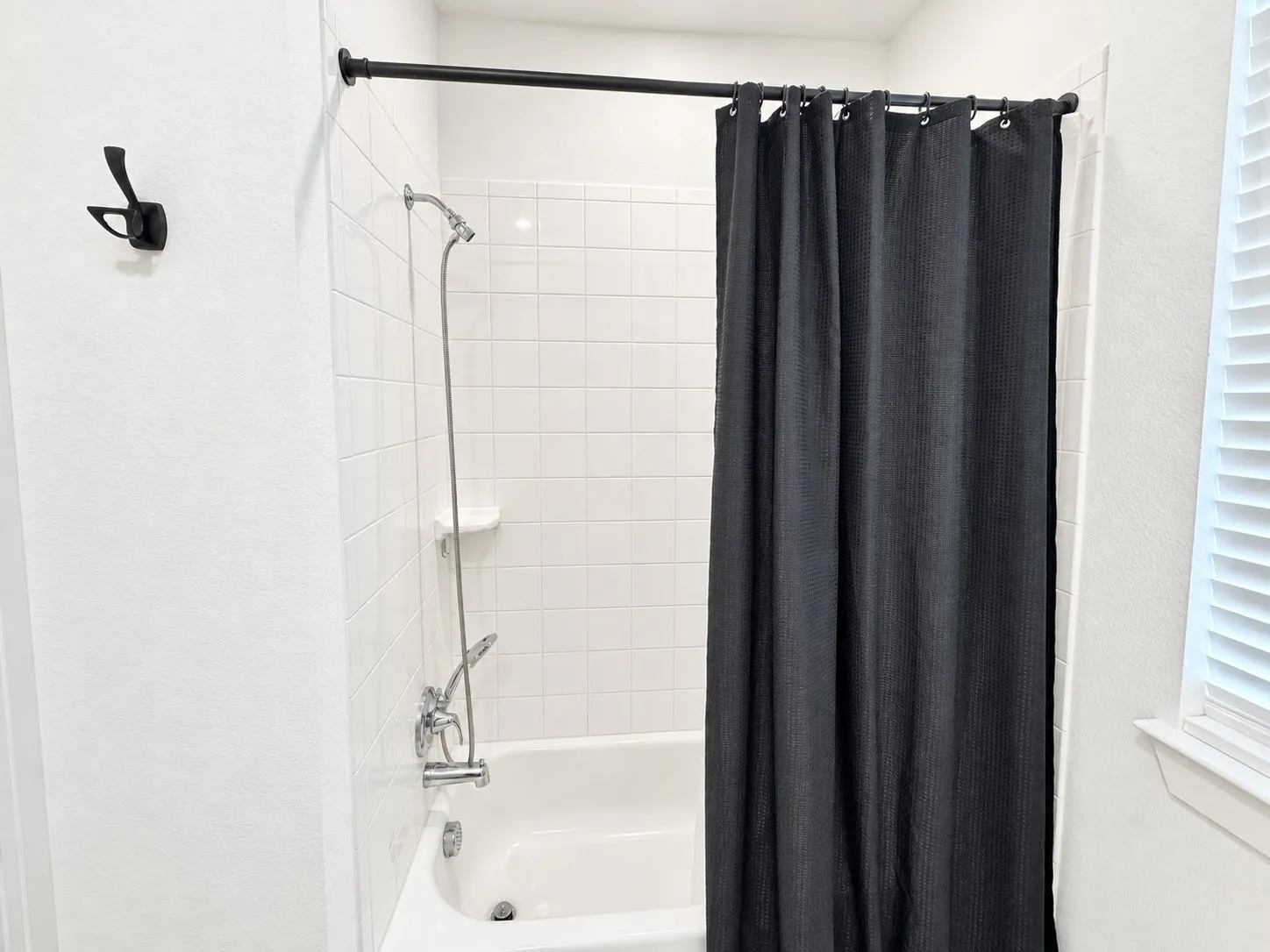 Bathtub with white tile surround, chrome fixtures, and a matte black shower rod