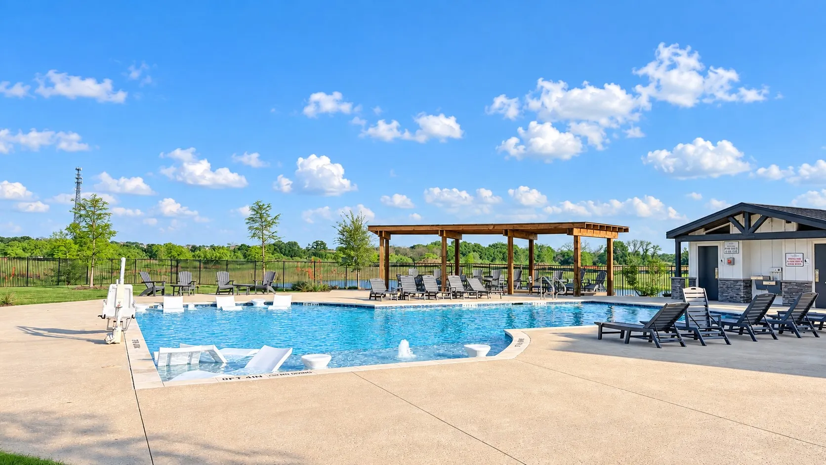 Swimming pool with concrete decking, a wooden pergola, and an adjacent structure with a stone facade