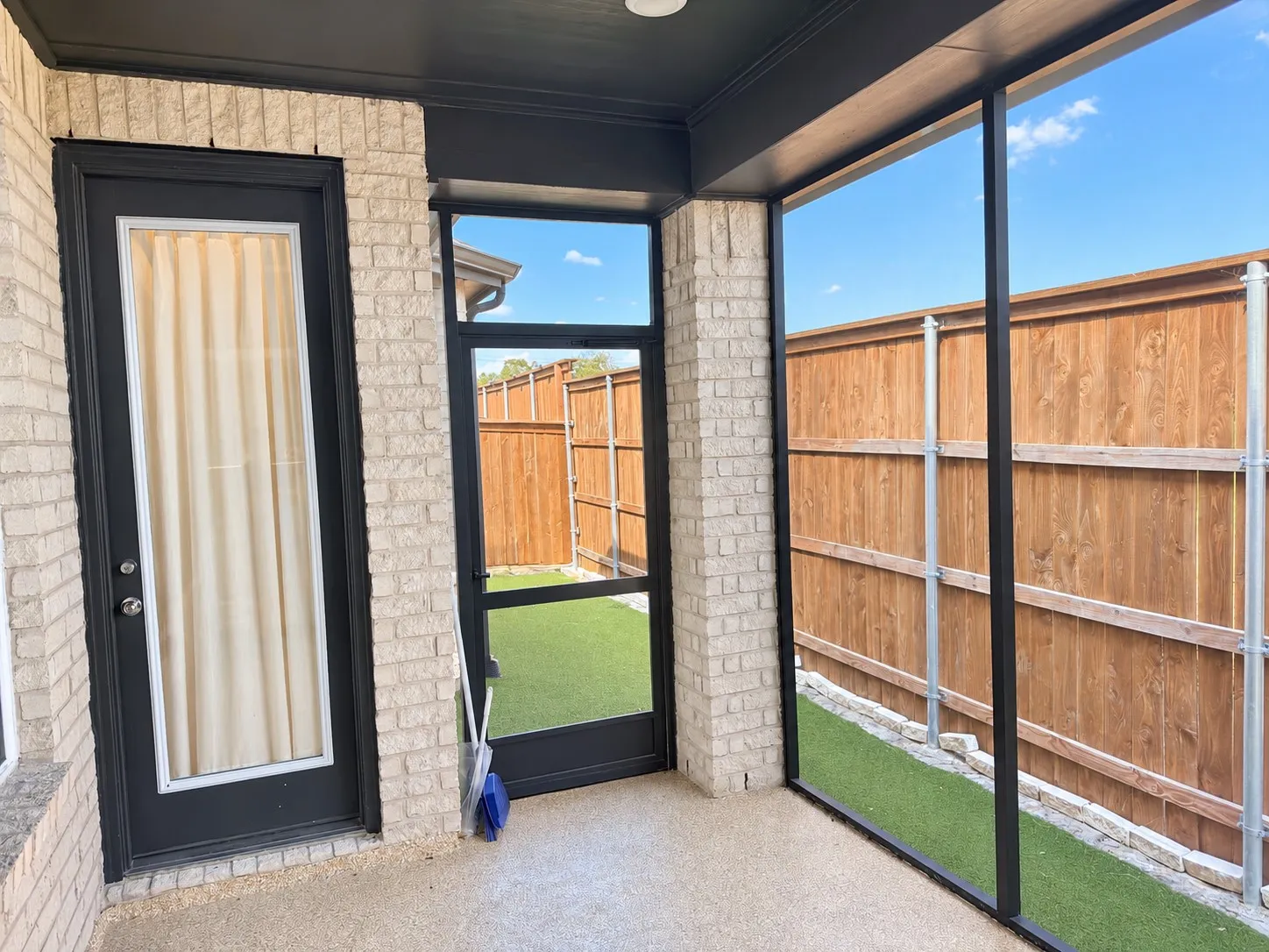 Screened-in patio featuring light brick exterior, dark trim, and a wood privacy fence