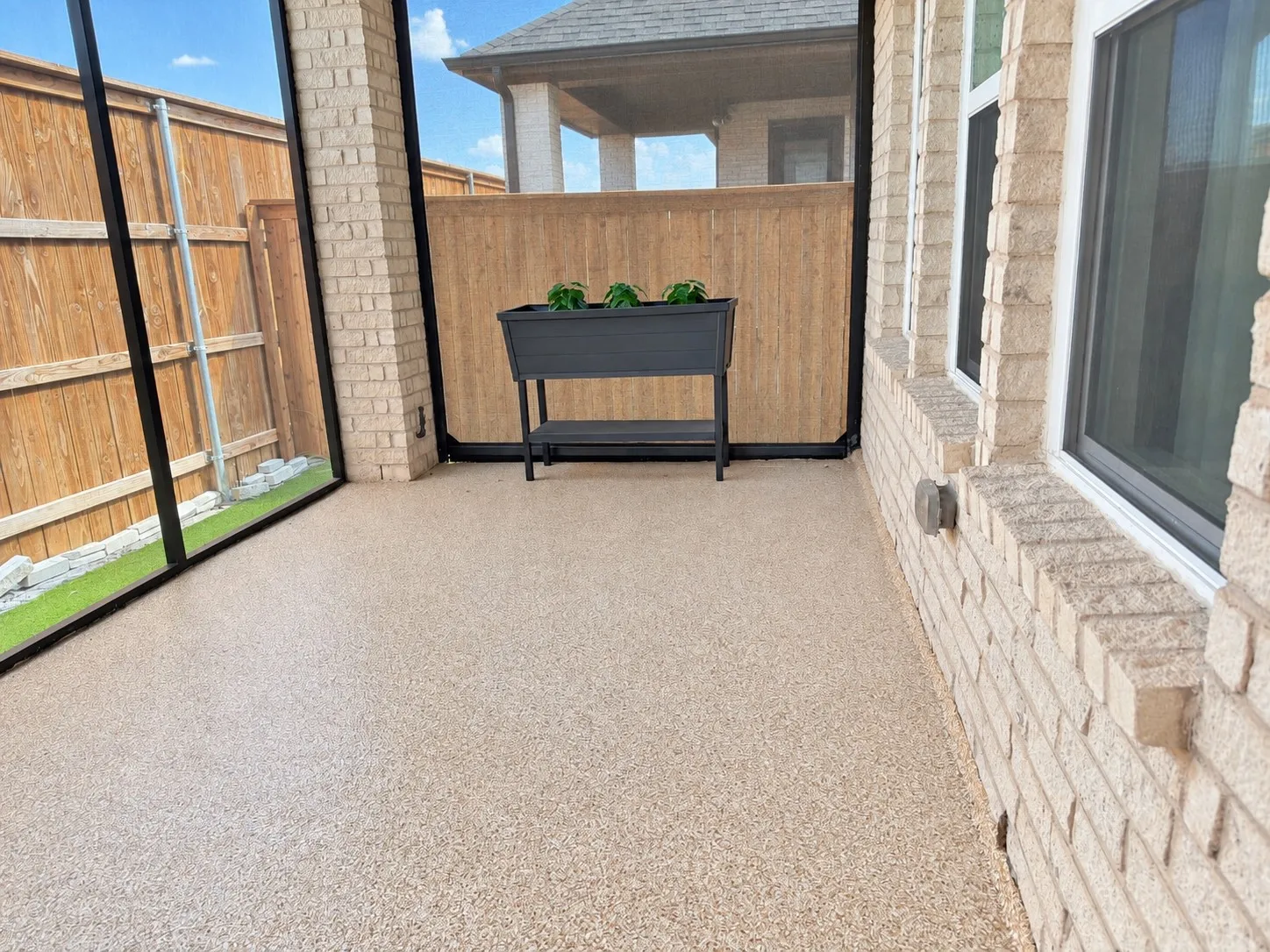 Screened outdoor living area with a textured flooring surface, brick exterior wall, and multiple windows