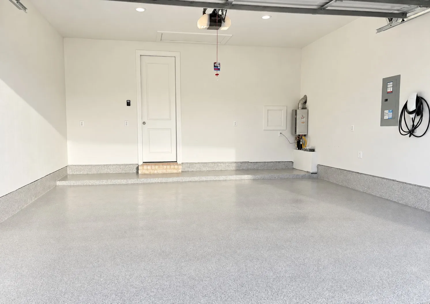Spacious garage featuring a durable epoxy floor, electric vehicle charging station, and tankless water heater