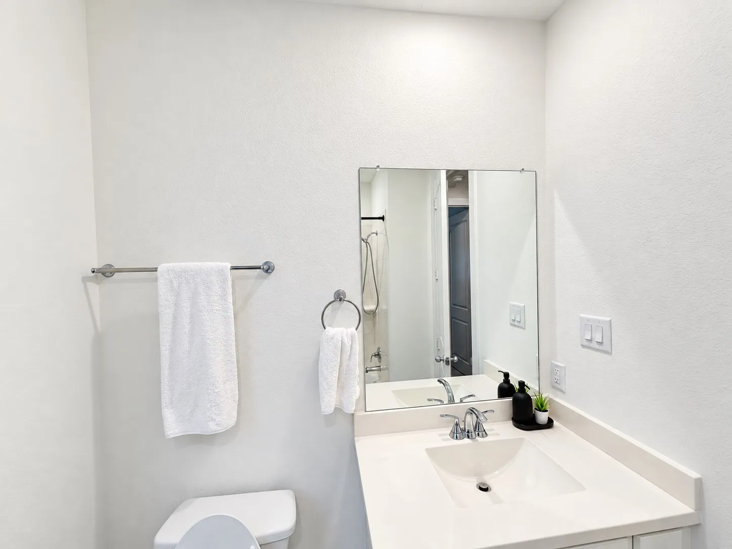 Vanity with an integrated sink and chrome faucet, rectangular wall-mounted mirror, and a toilet