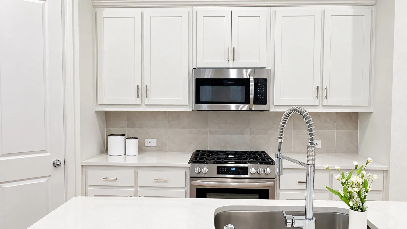 White shaker-style cabinetry, stainless steel appliances, light-toned backsplash, light-toned countertops, and a stainless steel sink with a high-arch faucet