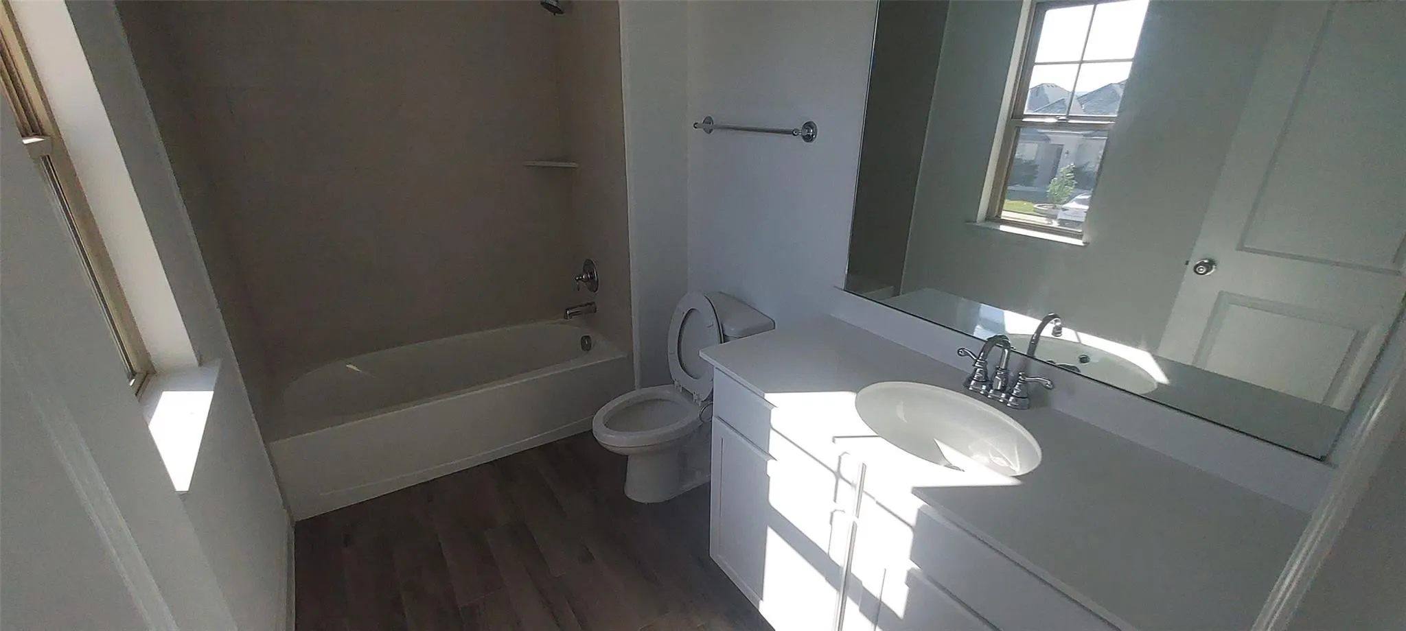 White vanity with chrome fixtures and a rectangular vessel sink, white bathtub, and wood-finish flooring