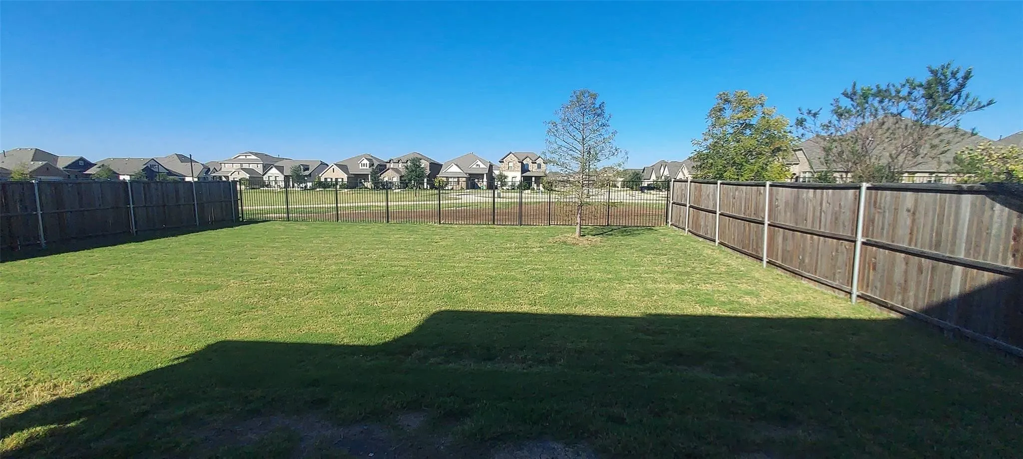 Expansive grassy yard area with a wood privacy fence and partial metal fencing
