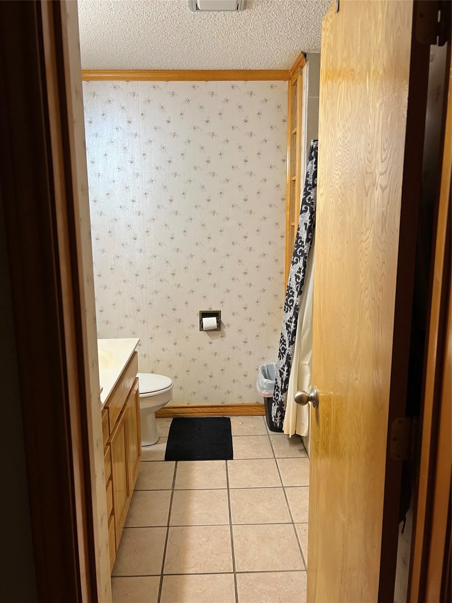 Bathroom featuring a vanity with light wood-finish cabinetry, a white toilet, and light-toned square tile flooring