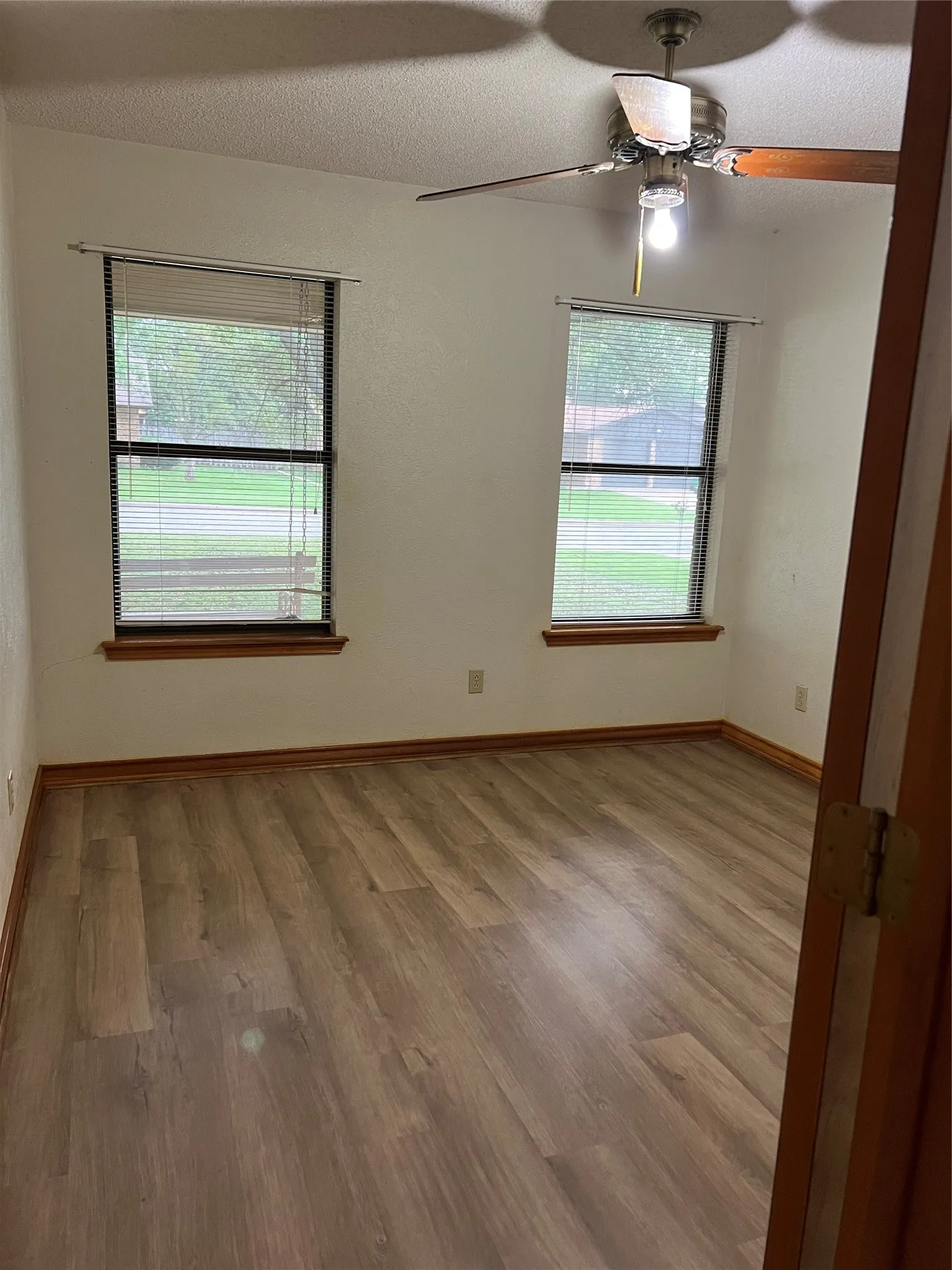 Wood-finish flooring throughout, two windows with blinds, and a ceiling fan with integrated lighting