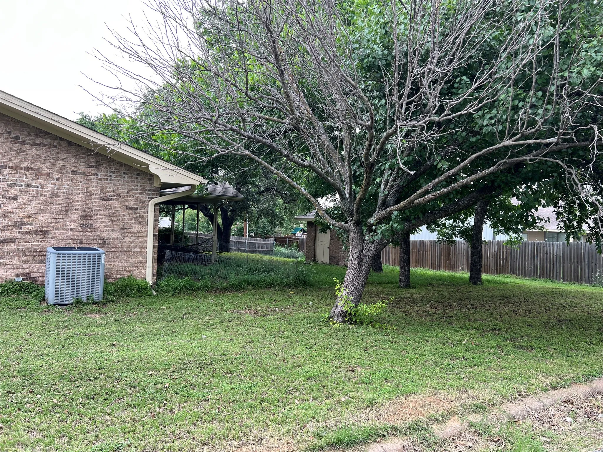 Brick exterior with a covered patio, mature trees, and a wooden privacy fence