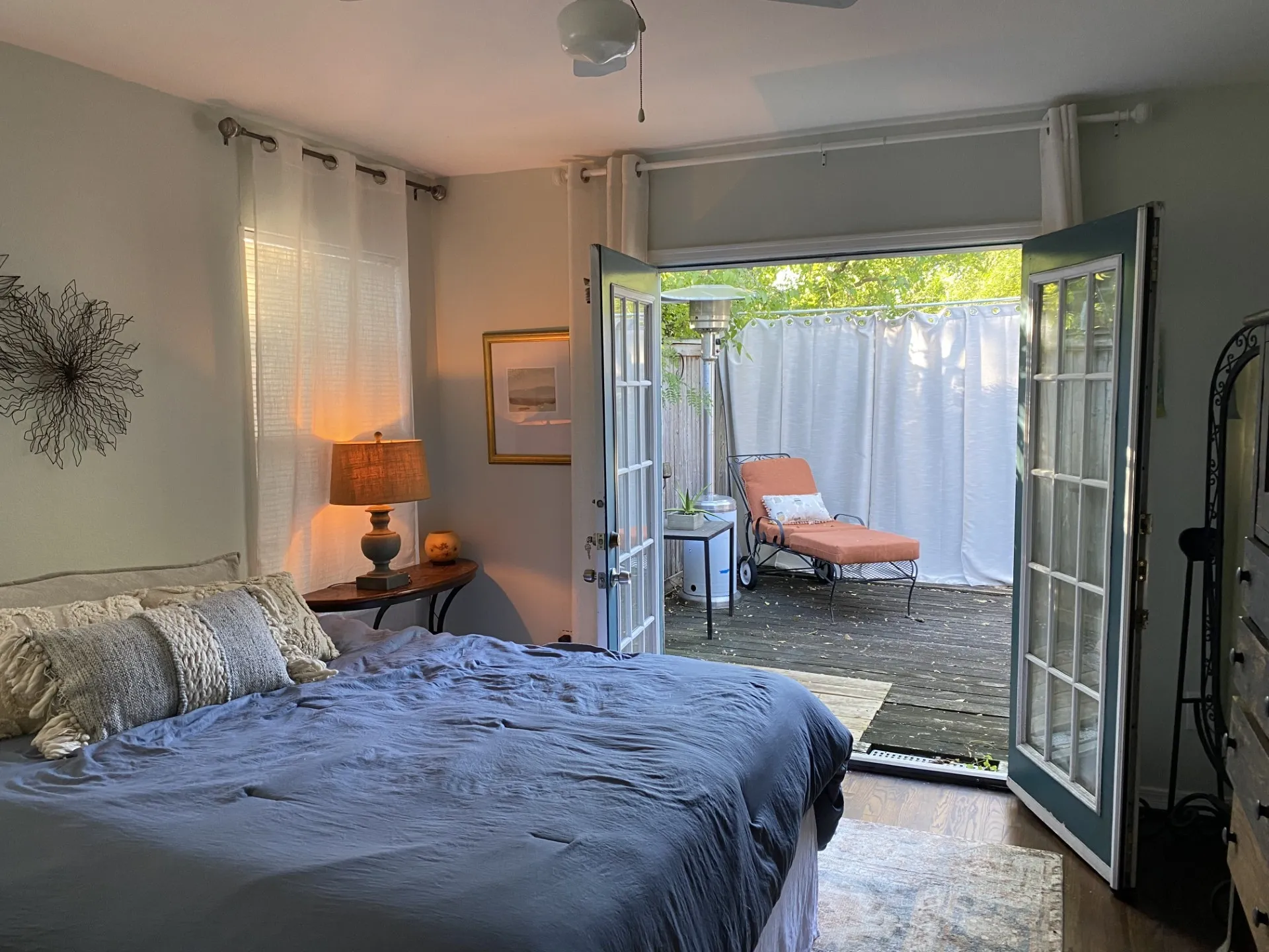 Hardwood-finish flooring, ceiling fan, and double French doors opening to an outdoor patio with privacy screening