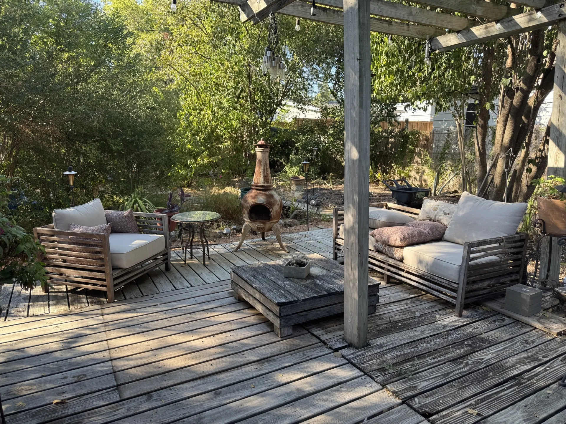 Wood-finish deck with a built-in pergola, string lighting, and mature perimeter landscaping
