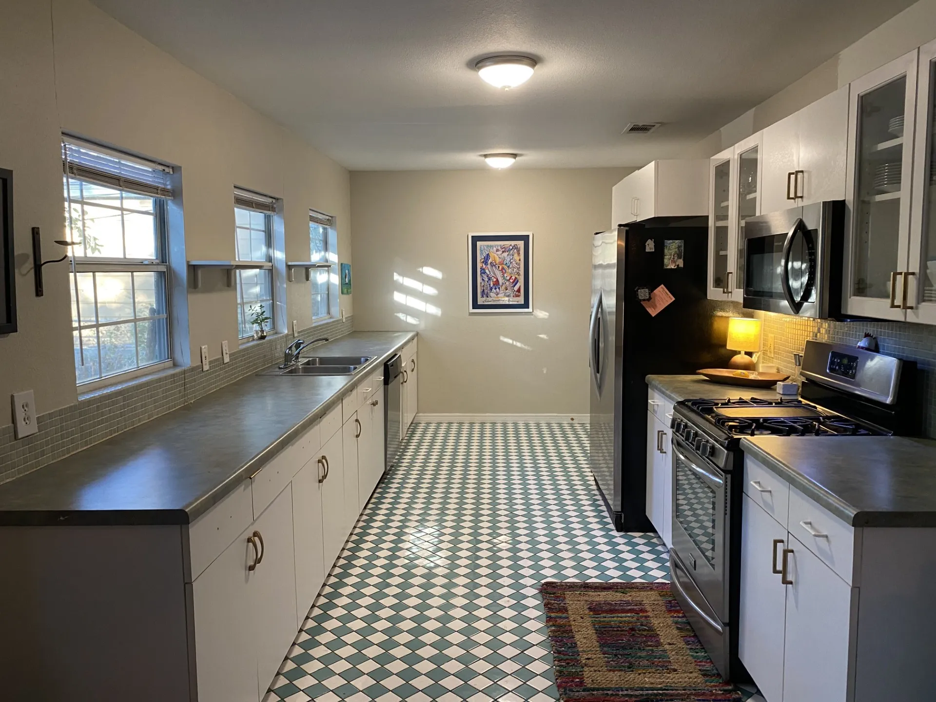 Kitchen featuring a checkered tile floor, multiple windows, a tile backsplash, white cabinetry, and stainless steel appliances