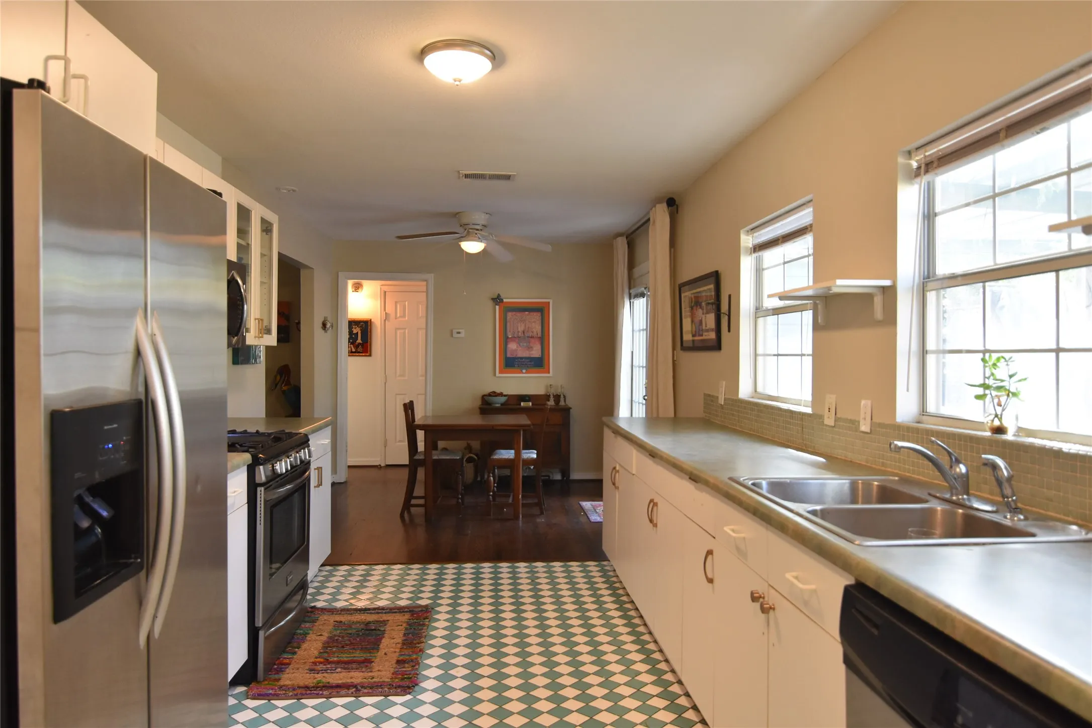Kitchen featuring a stainless steel refrigerator, stainless steel range, white cabinetry, double basin sink, and tiled backsplash